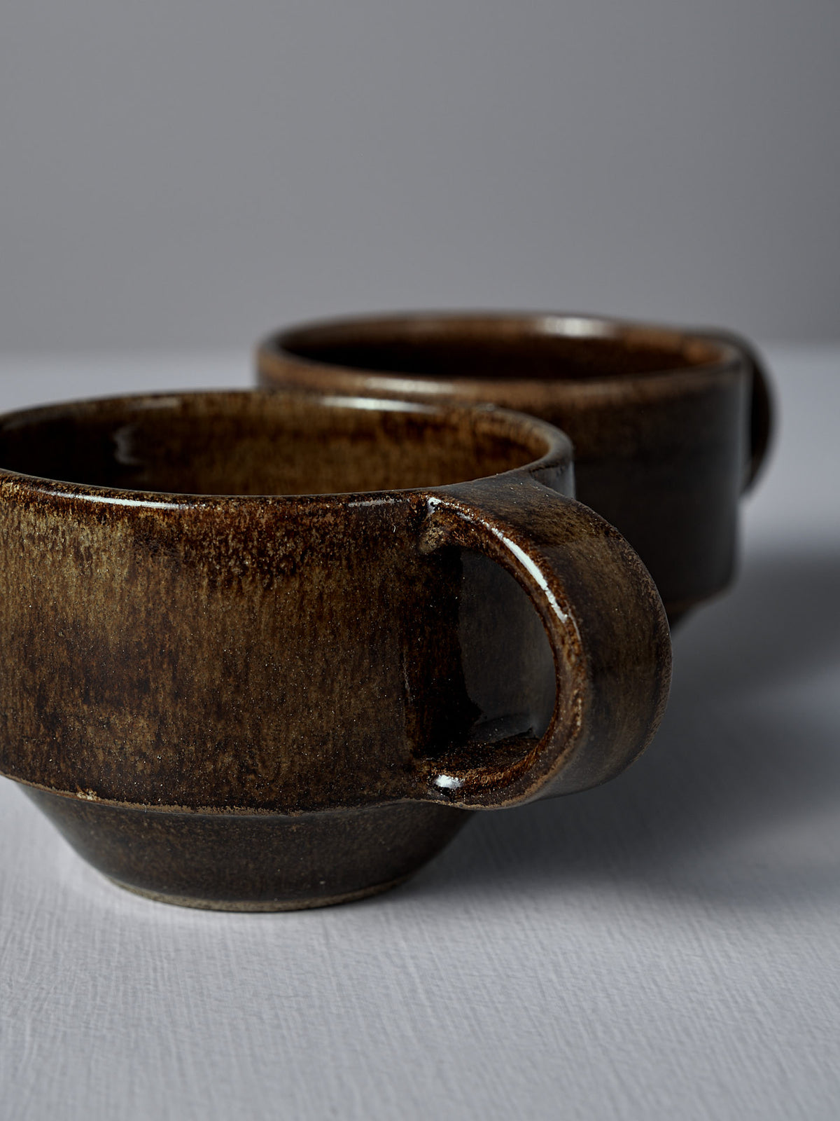 Two Studio Foon Everyday Stacker Cups – Small in Burnt Umber, featuring large handles and handcrafted design, are placed on a plain white surface against a neutral background—ideal for your daily coffee.