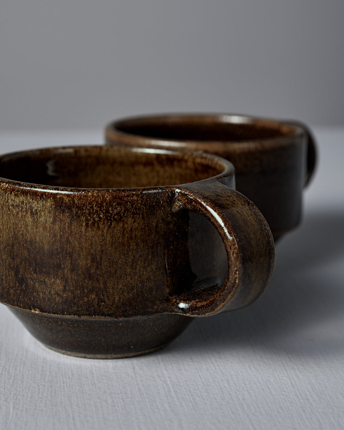 Two Studio Foon Everyday Stacker Cups – Small in Burnt Umber, featuring large handles and handcrafted design, are placed on a plain white surface against a neutral background—ideal for your daily coffee.