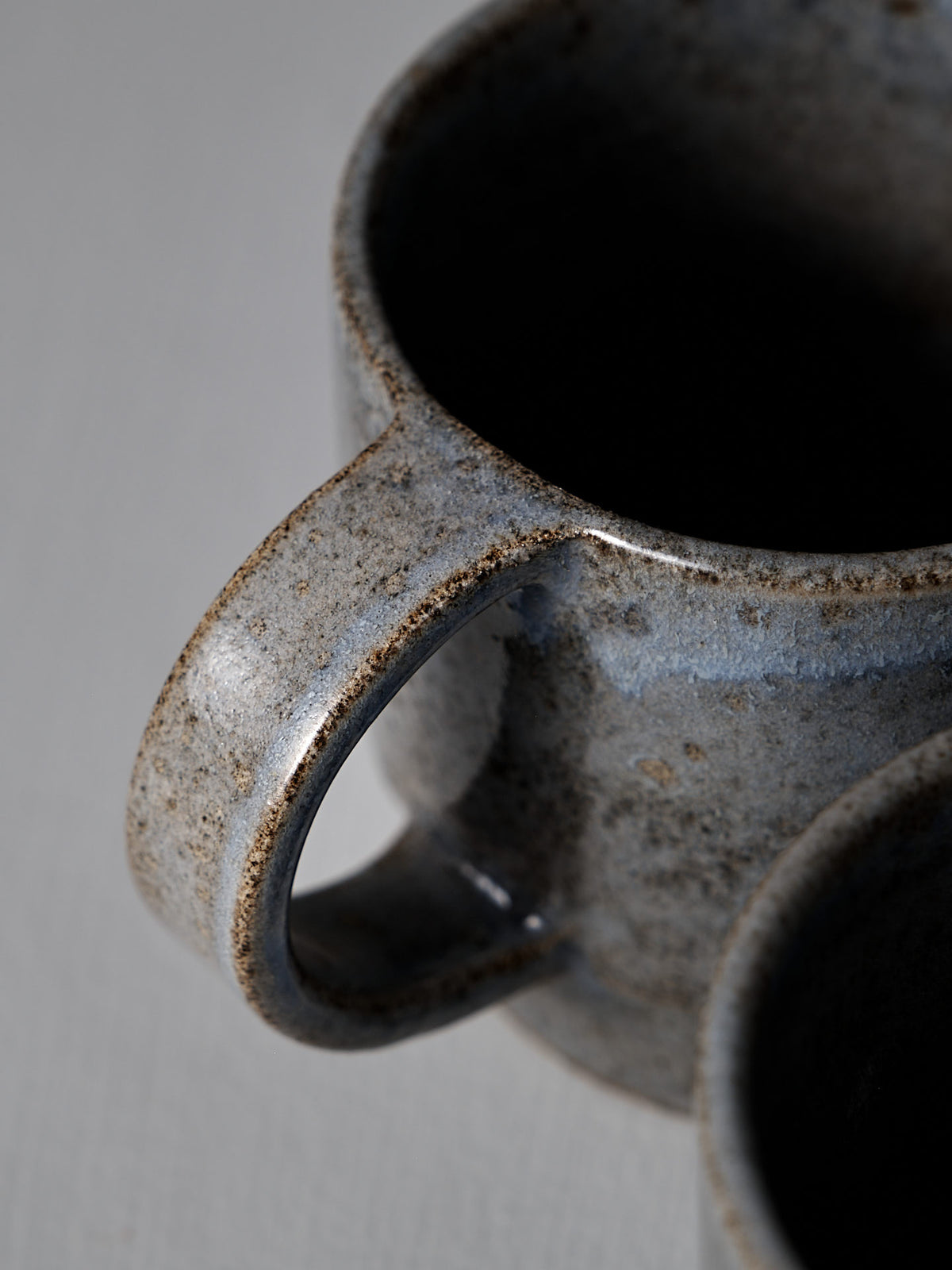 Close-up of the Studio Foon Everyday Stacker Cup – Large in Indigo, showing its textured handle and speckled glaze, partially overlapping another mug on a light surface.