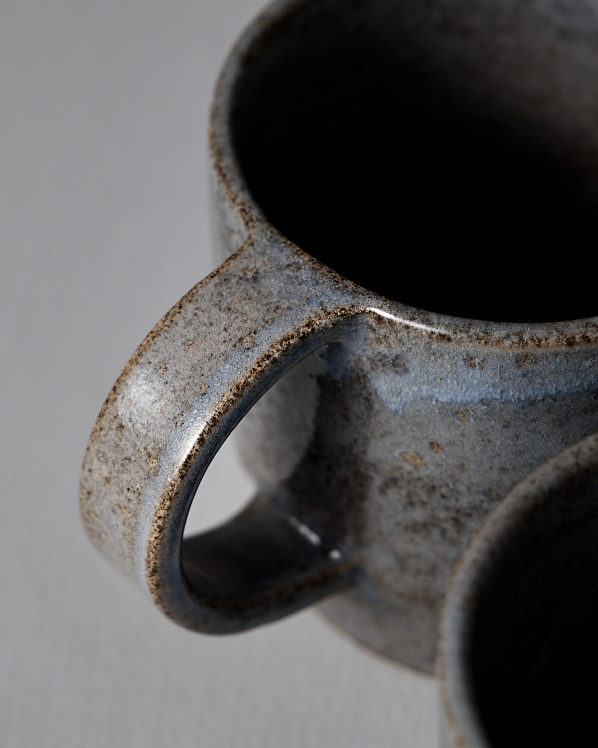 Close-up of the Studio Foon Everyday Stacker Cup – Large in Indigo, showing its textured handle and speckled glaze, partially overlapping another mug on a light surface.