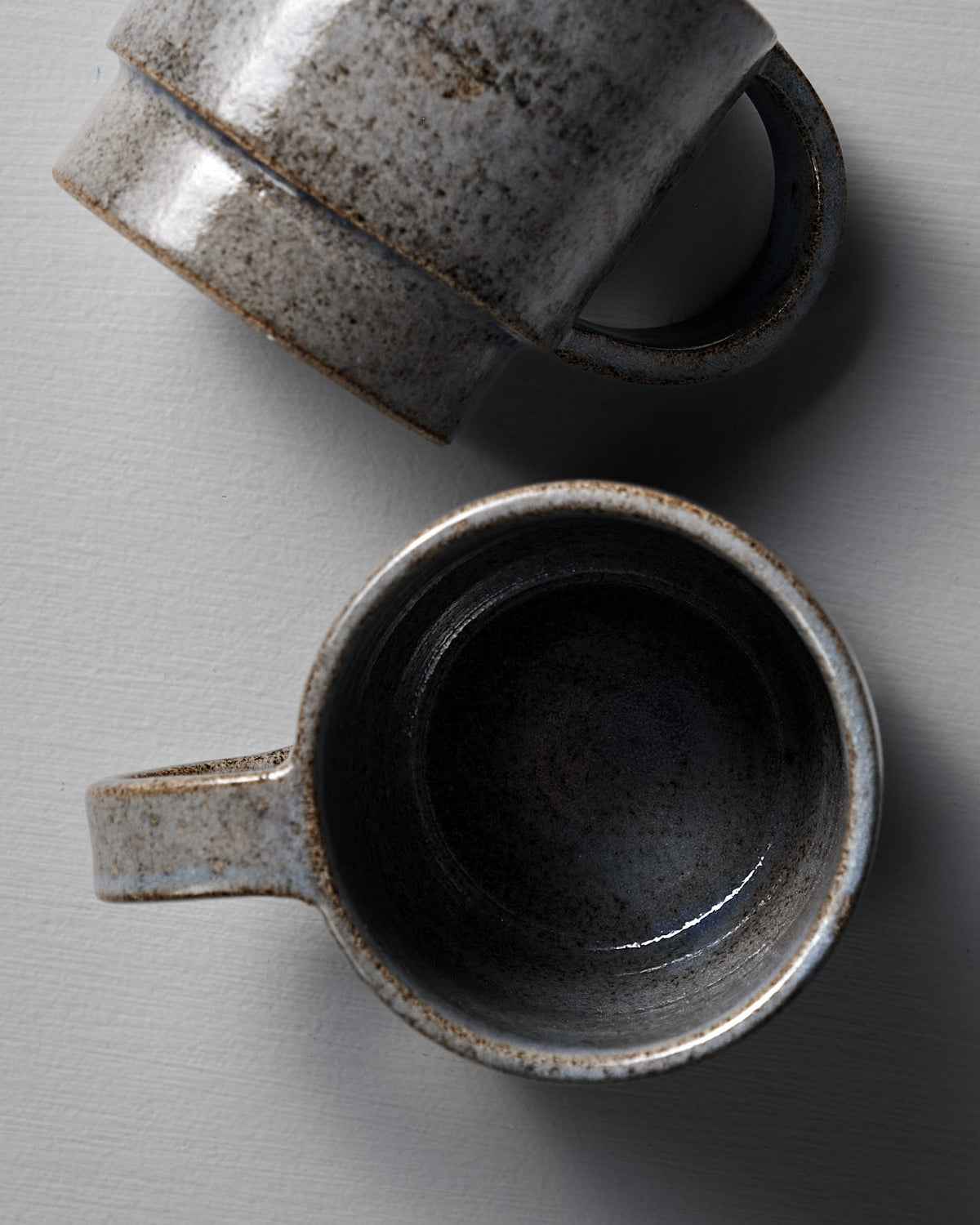 Two Everyday Stacker Cup – Large | Indigo mugs by Studio Foon, one upright and one on its side, display their charm as perfect everyday cups on a light textured surface.