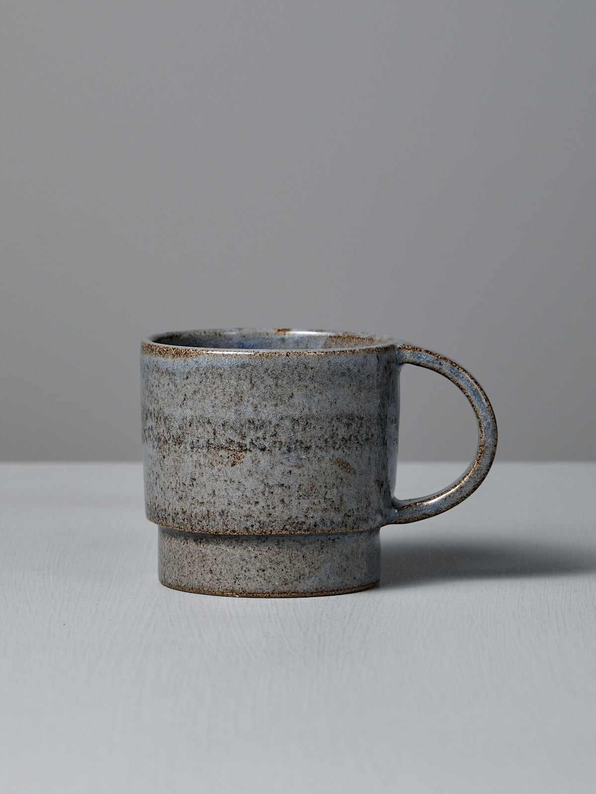 The Studio Foon Everyday Stacker Cup – Large | Indigo (300ml), handcrafted with a speckled gray and brown finish, is displayed on a light surface against a plain gray background.