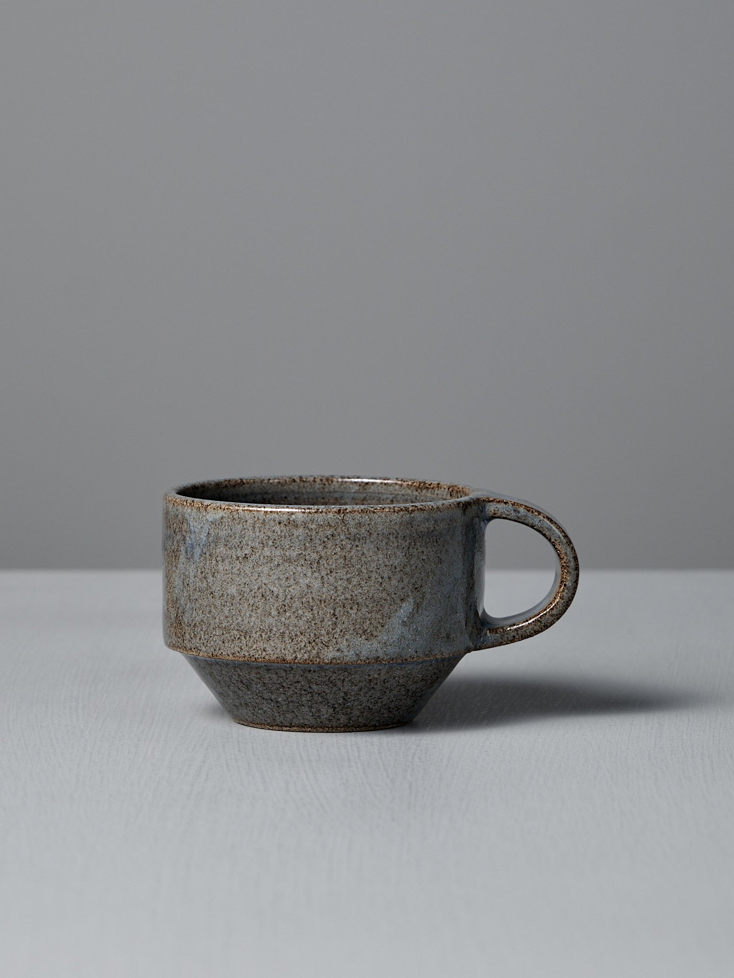 The Studio Foon Everyday Stacker Cup – Small in Indigo, featuring a handcrafted textured finish, rests on a light gray surface against a plain gray background.