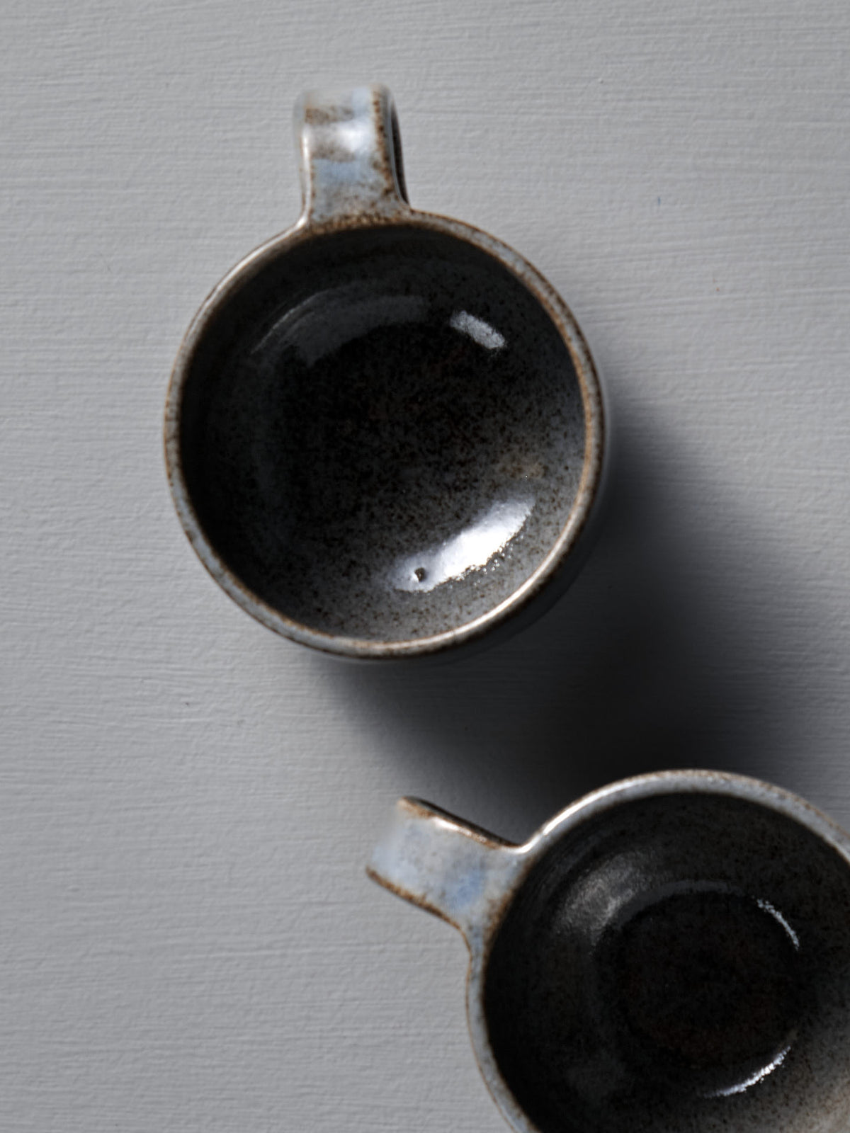 Two Everyday Stacker Cups – Small in Indigo from Studio Foon, with handles, are seen from above, stacked on a light gray textured surface.