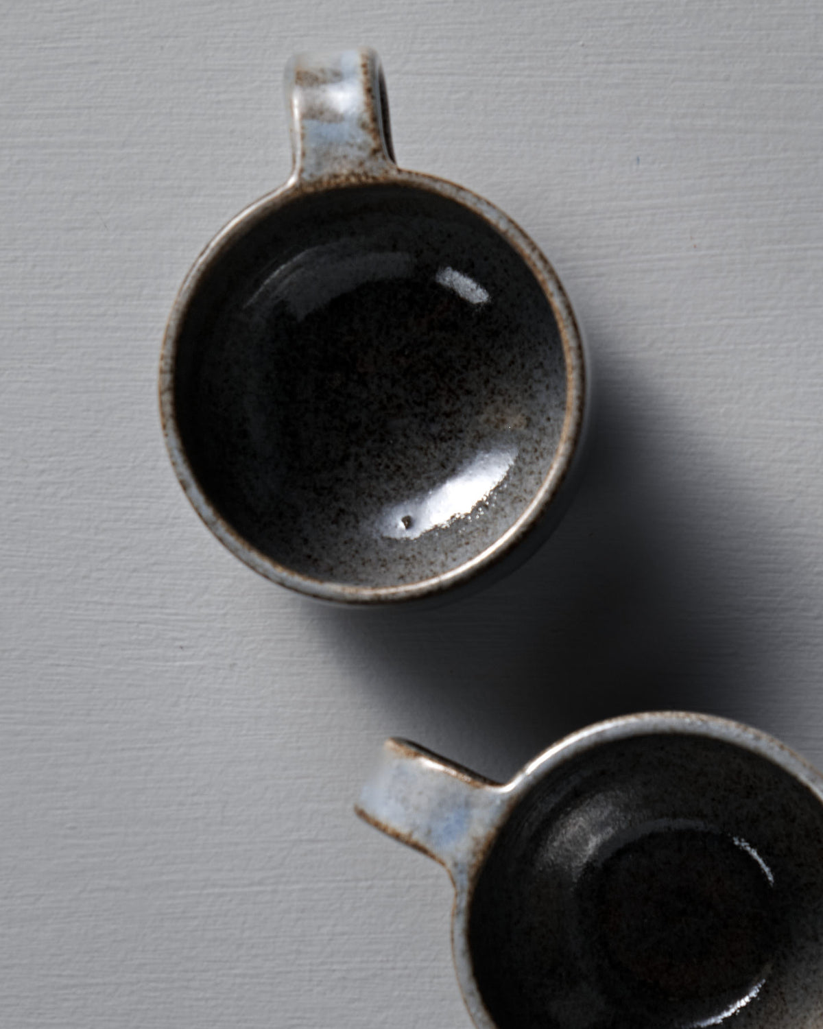 Two Everyday Stacker Cups – Small in Indigo from Studio Foon, with handles, are seen from above, stacked on a light gray textured surface.