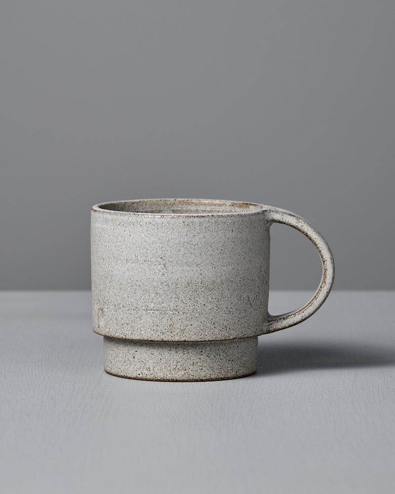 The Studio Foon Everyday Stacker Cup – Large | Stone White is a handcrafted, speckled 300ml cup with a large handle. It’s perfect for daily use and pairs well with other stackable cups on any light gray surface.