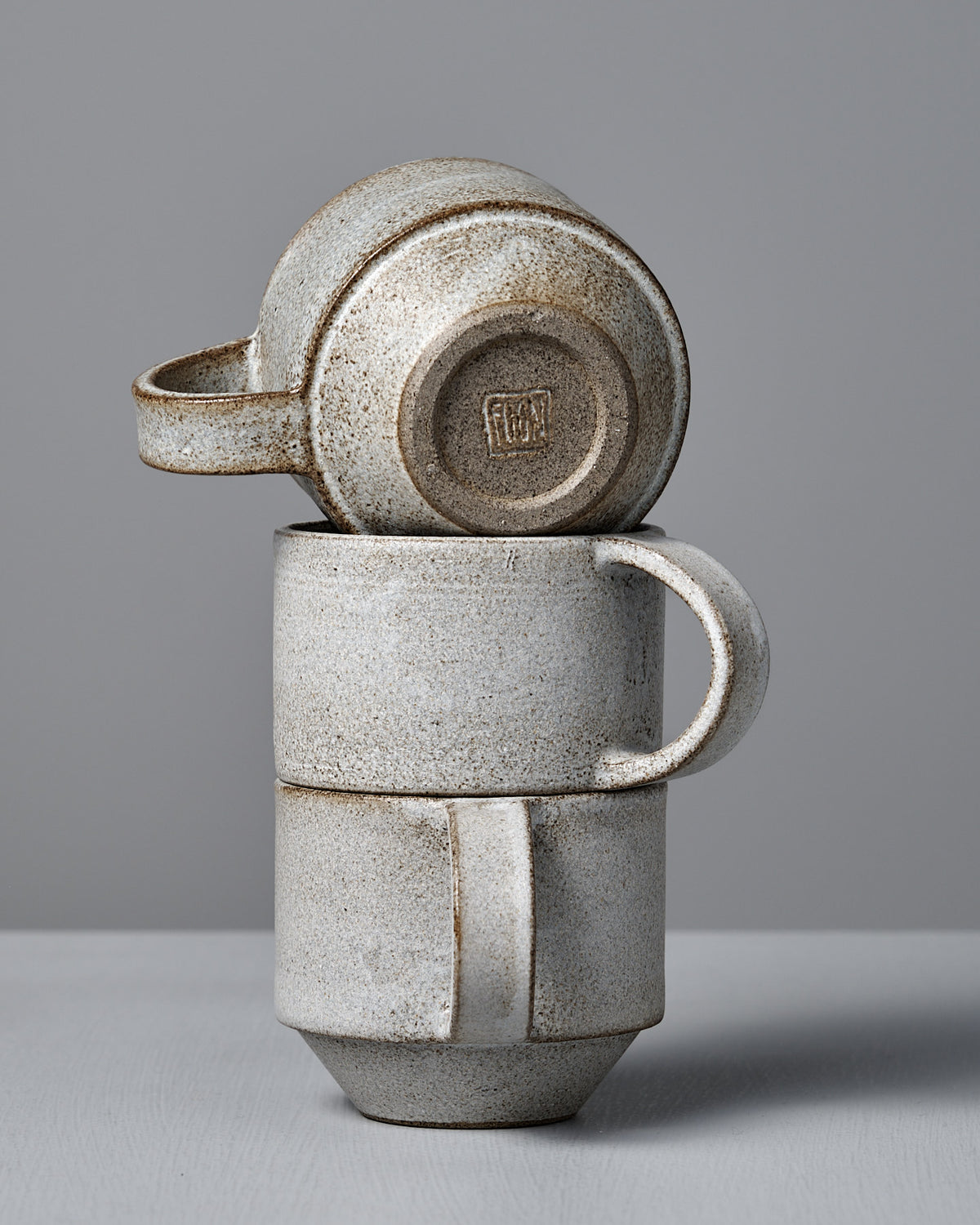 Two Studio Foon Everyday Stacker Cups – Medium in Stone White are stacked on a gray surface, highlighting their stackable design.