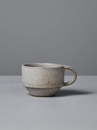 The Studio Foon Everyday Stacker Cup – Small in Stone White features a matte, speckled light gray finish with a handle, resting on a matching surface—ideal for your daily coffee ritual.