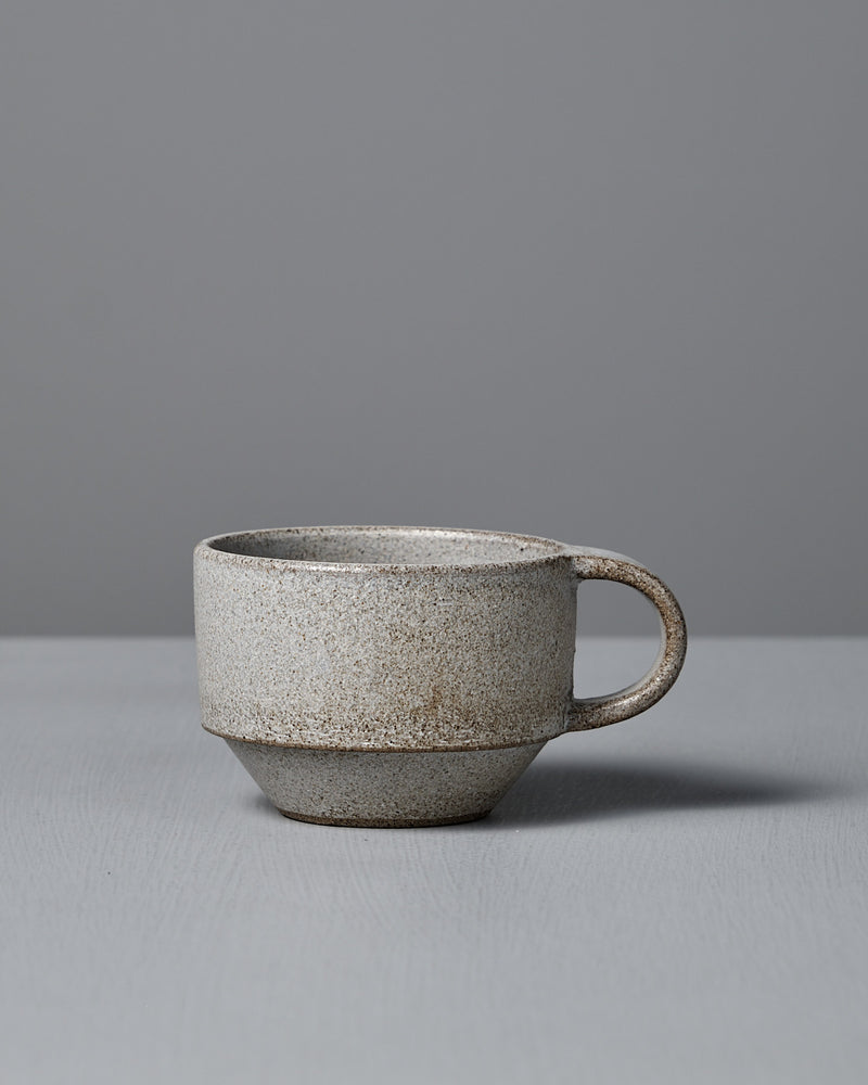 The Studio Foon Everyday Stacker Cup – Small in Stone White features a matte, speckled light gray finish with a handle, resting on a matching surface—ideal for your daily coffee ritual.