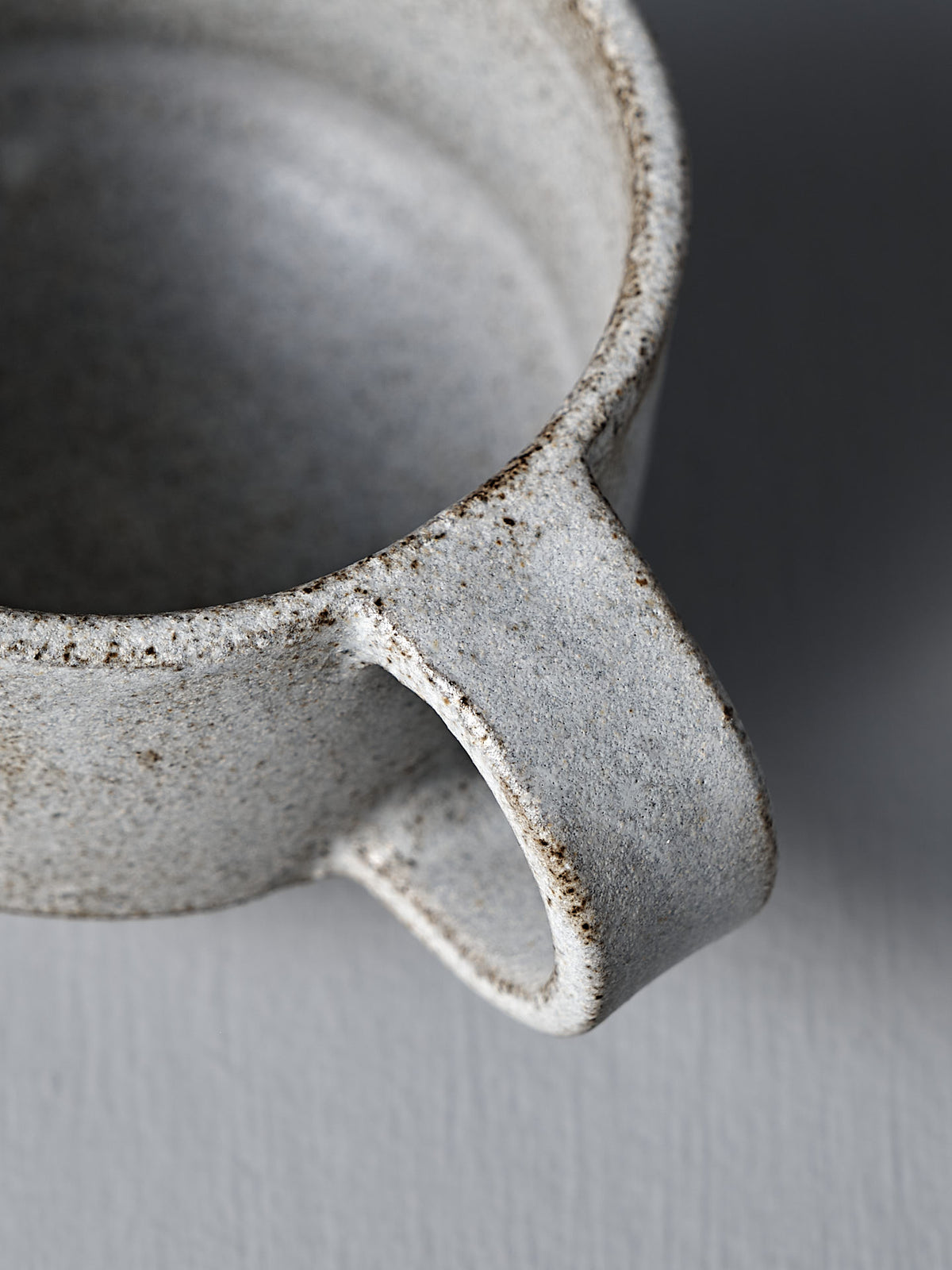 Close-up of the Studio Foon Everyday Stacker Cup – Small in Stone White, featuring a textured, speckled glaze and thick handle—ideal for enjoying unique, handcrafted mugs in your daily routine—set against a gray background.