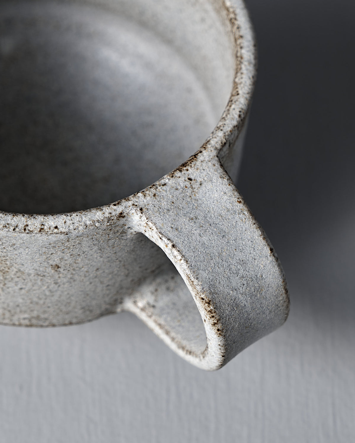 Close-up of the Studio Foon Everyday Stacker Cup – Small in Stone White, featuring a textured, speckled glaze and thick handle—ideal for enjoying unique, handcrafted mugs in your daily routine—set against a gray background.