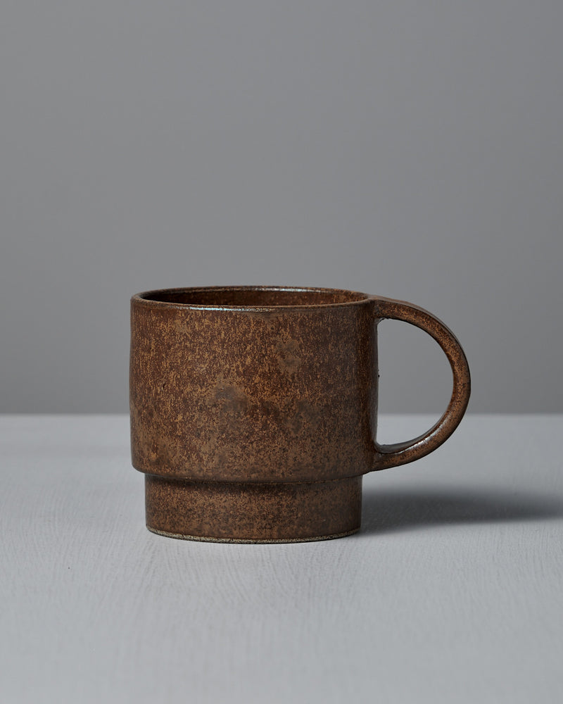 The Studio Foon Everyday Stacker Cup – Large in terracotta, featuring a rounded handle, is ideal for daily collections and is displayed on a light gray surface against a plain gray background.
