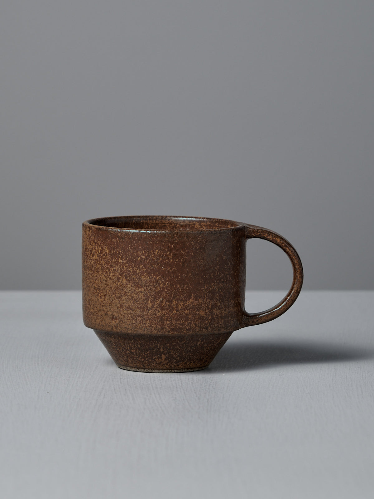 The Studio Foon Everyday Stacker Cup – Medium in Terracotta features a matte, textured ceramic finish and sits on a light gray surface against a gray background—ideal for daily coffee rituals.