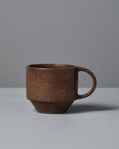 The Studio Foon Everyday Stacker Cup – Medium in Terracotta features a matte, textured ceramic finish and sits on a light gray surface against a gray background—ideal for daily coffee rituals.