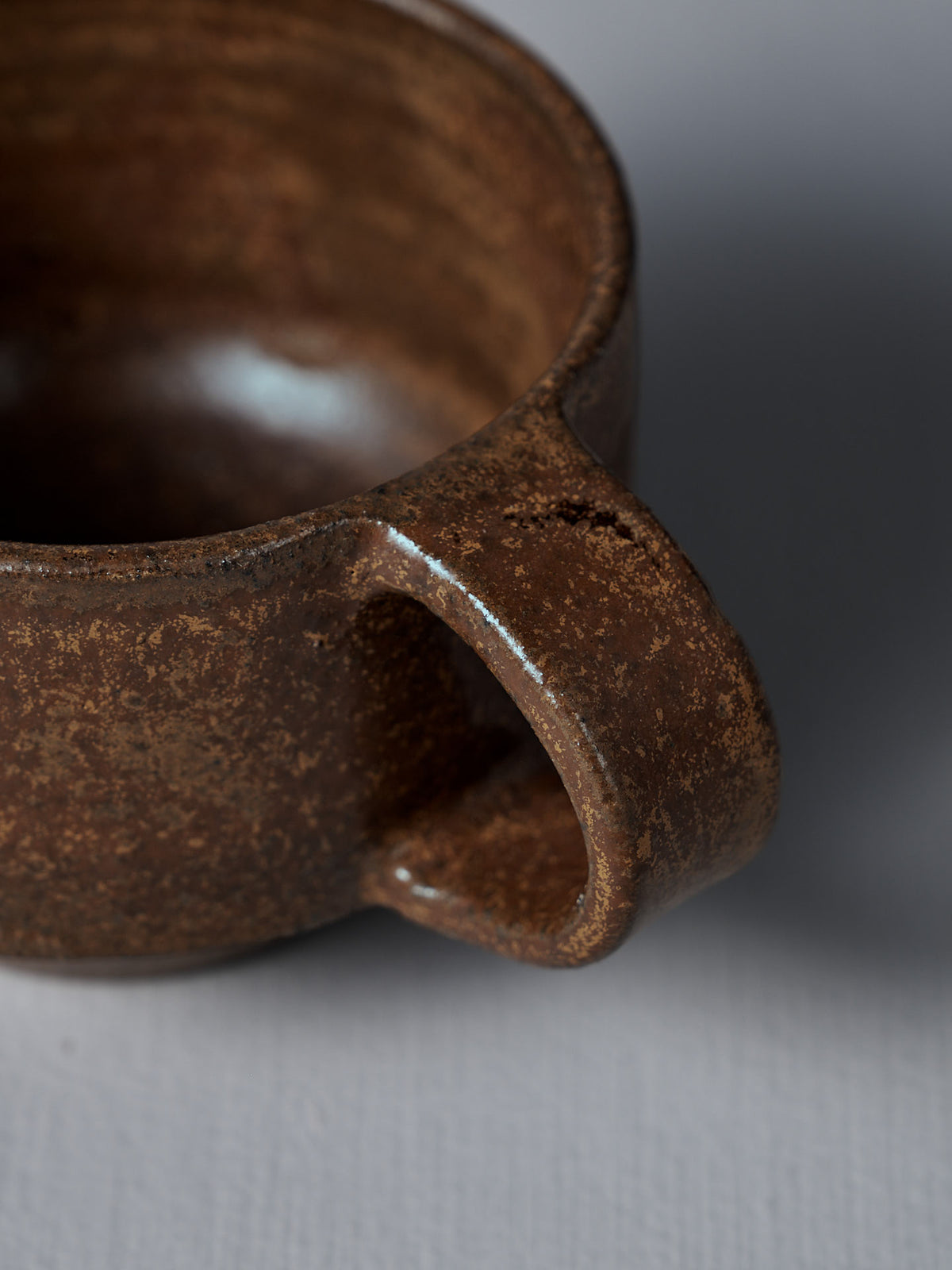 Close-up of the Studio Foon Everyday Stacker Cup – Small in Terracotta, highlighting its textured ceramic surface, handle, and rim against a plain gray background.