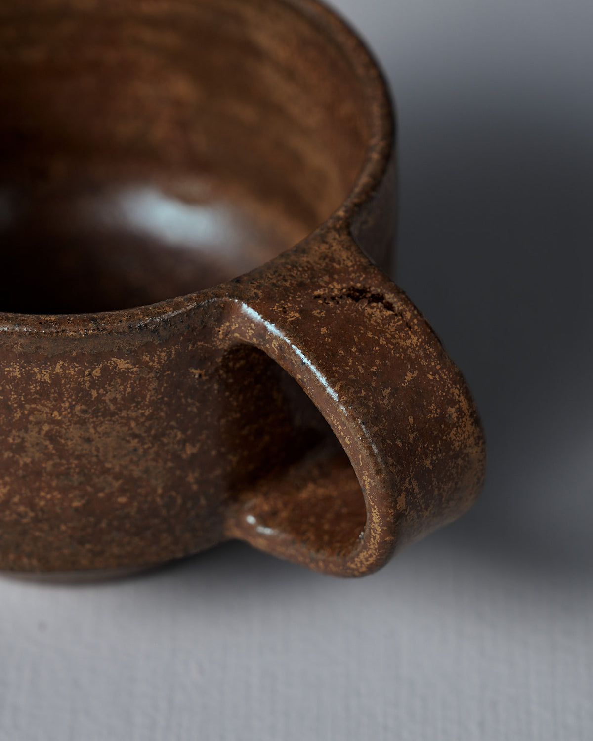 Close-up of the Studio Foon Everyday Stacker Cup – Small in Terracotta, highlighting its textured ceramic surface, handle, and rim against a plain gray background.