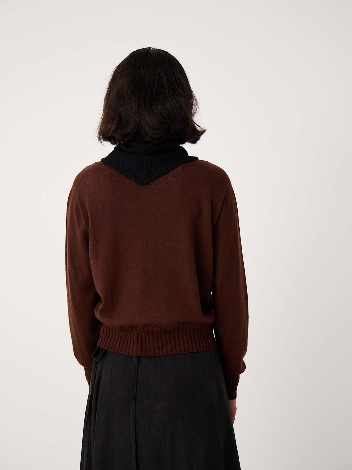 A person with short dark hair, seen from behind, wears a brown sweater, dark skirt, and the Daisy Scarf – Black while standing on an extra wide yoga mat against a plain light background.