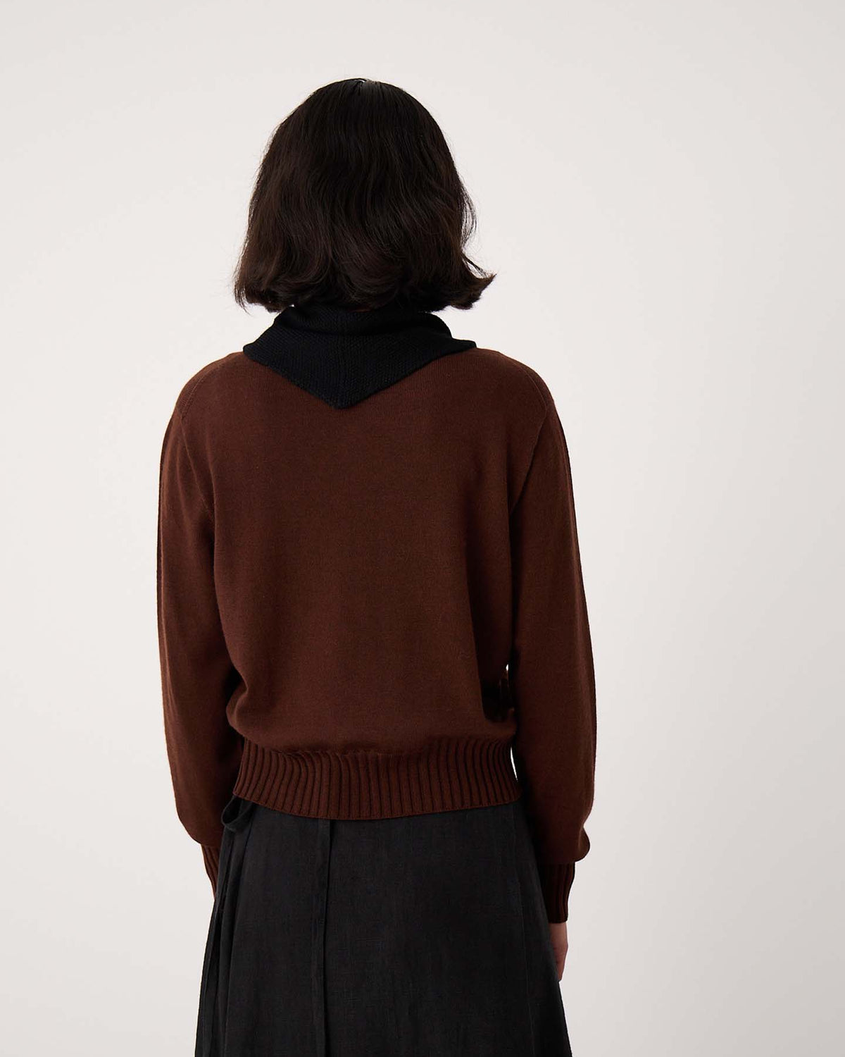 A person with short dark hair, seen from behind, wears a brown sweater, dark skirt, and the Daisy Scarf – Black while standing on an extra wide yoga mat against a plain light background.