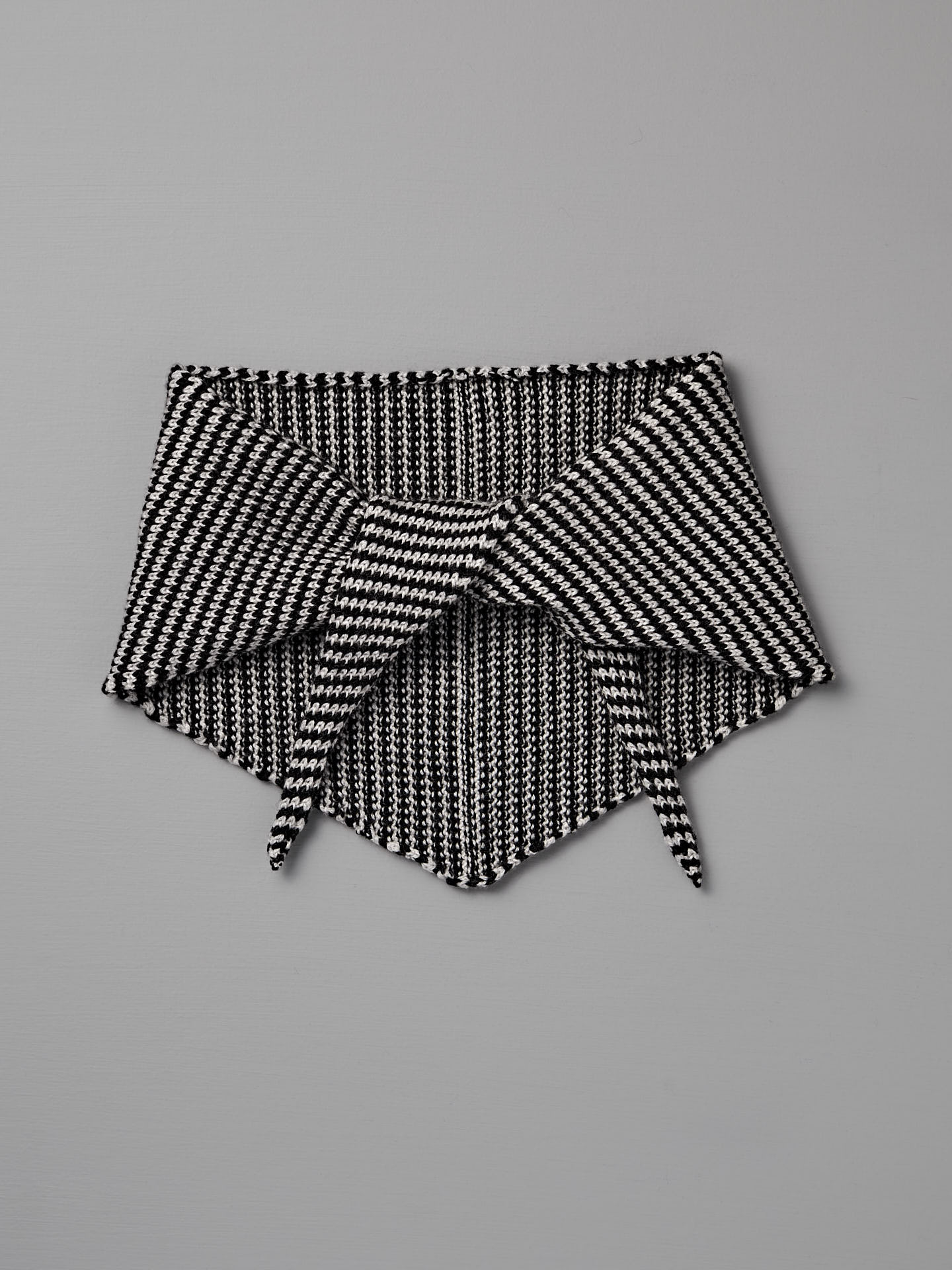 The Daisy Scarf – Black & Creme Stripe features a geometric knit pattern in black and creme, shown flat on a gray background with pointed ends overlapping. Dimensions: 97cm long x 22cm wide.