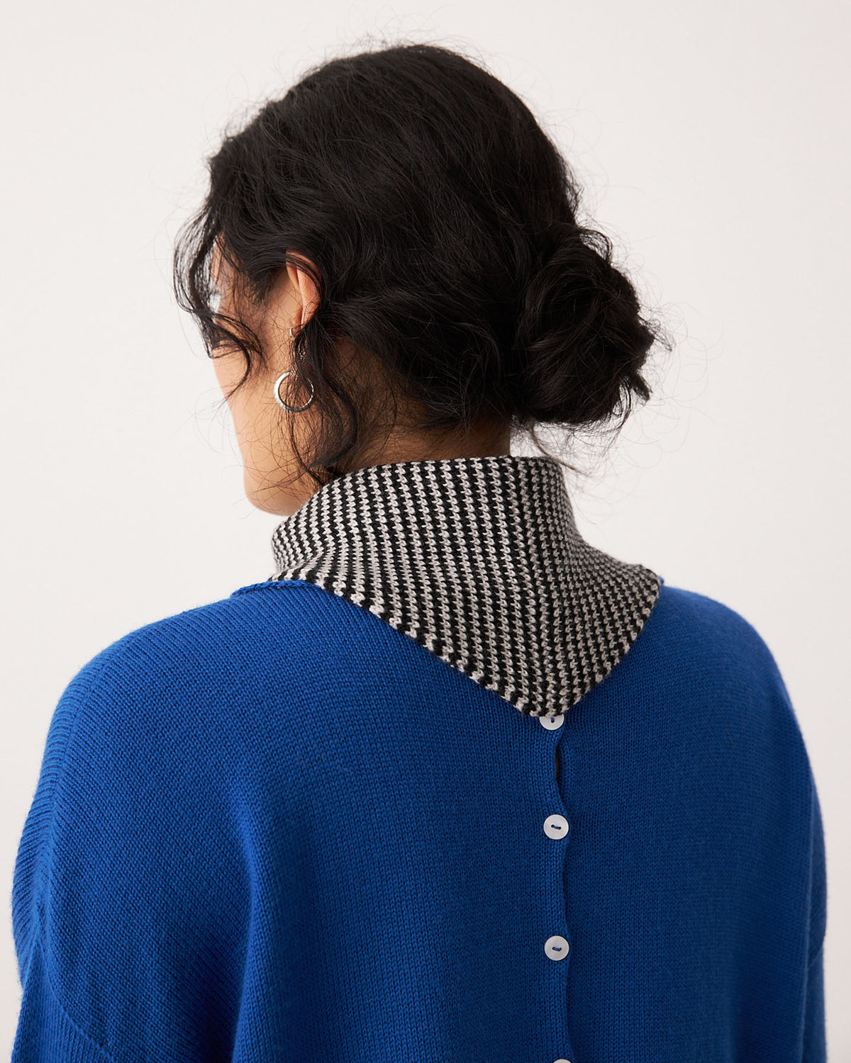 A person with dark hair in a low bun, shown from behind against a plain background, wears the Daisy Scarf in Black & Creme Stripe and a blue sweater with back buttons and houndstooth collar (approx. 97cm long).
