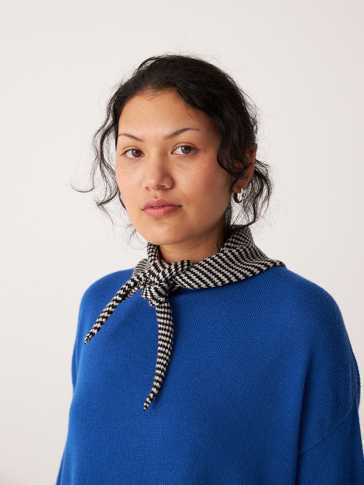 A person wearing a blue sweater and the Francie Daisy Scarf – Black Stripe (97cm x 22cm), standing against a plain light background.