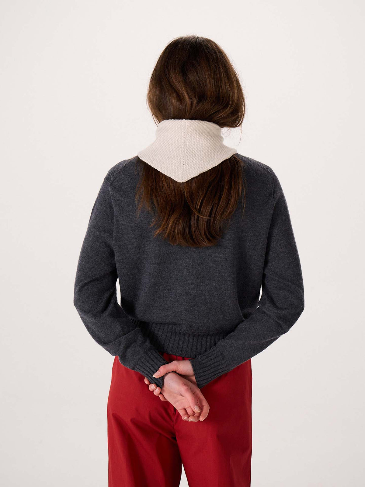 A person with long brown hair, wearing a gray sweater, red pants, and the Daisy Scarf in Ivory, stands with their back to the camera and hands clasped behind them on a wide fitness mat.