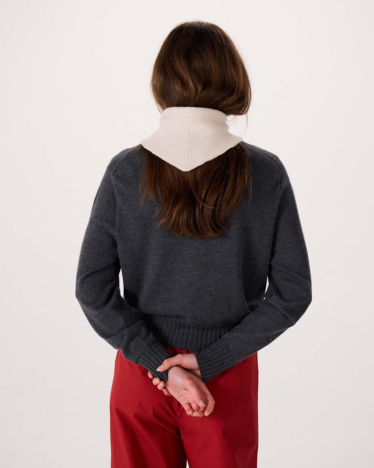 A person with long brown hair, wearing a gray sweater, red pants, and the Daisy Scarf in Ivory, stands with their back to the camera and hands clasped behind them on a wide fitness mat.