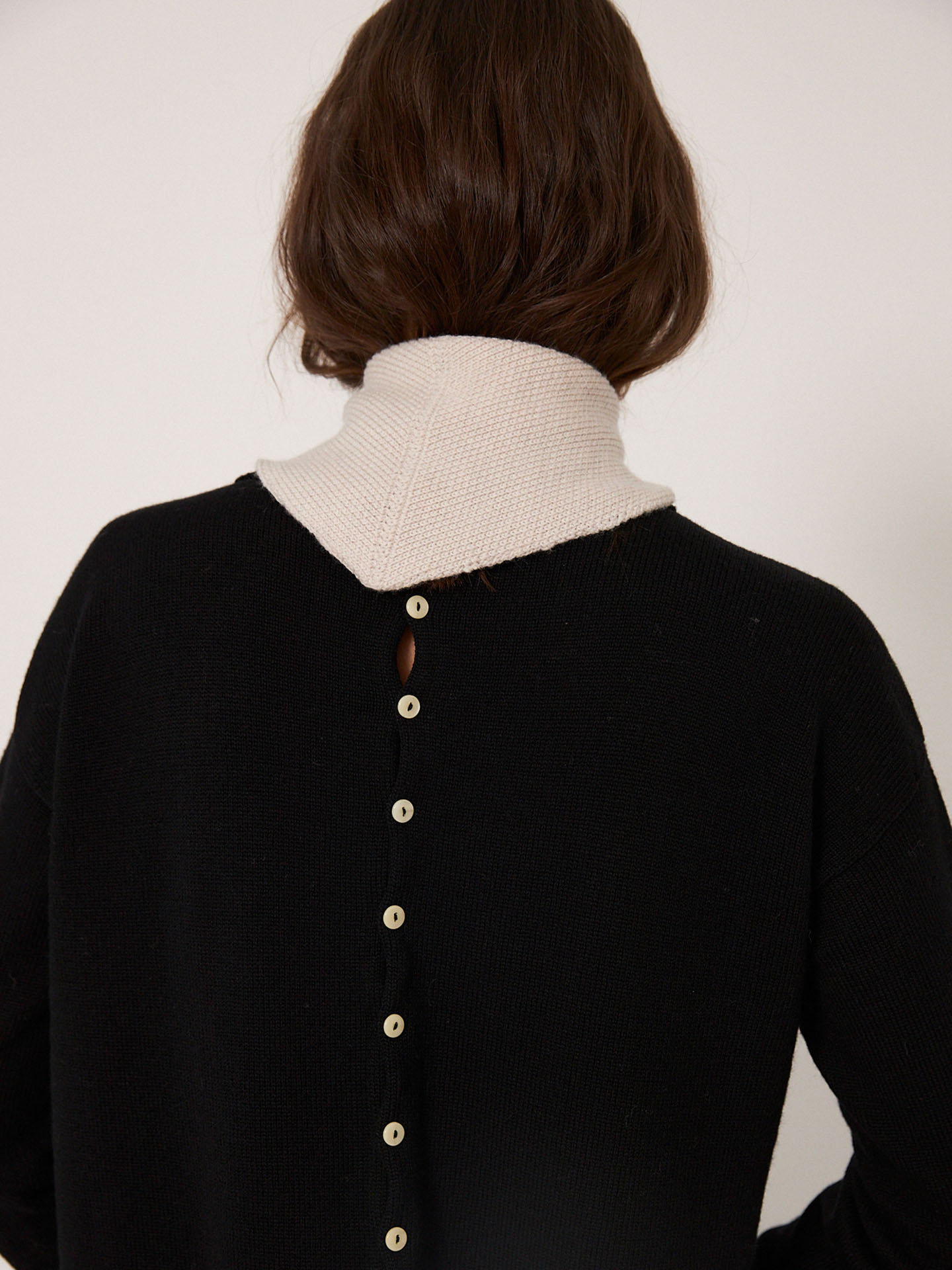A person with medium-length brown hair is shown from behind wearing the Francie Daisy Scarf in Ivory, styled over a black top. The scarf measures 97cm long and 22cm wide at its widest point.