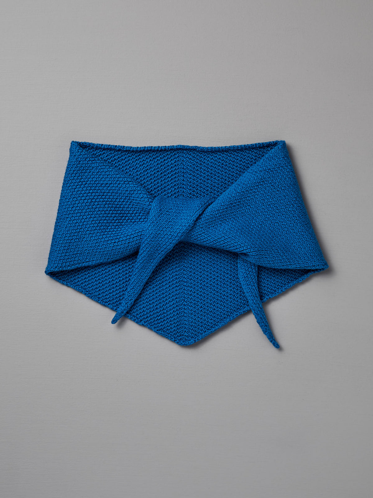 The Daisy Scarf – Azure by Francie features soft blue knit with pointed ends and a center tie, shown on a grey background—ideal for staying cozy after yoga on an extra wide mat.