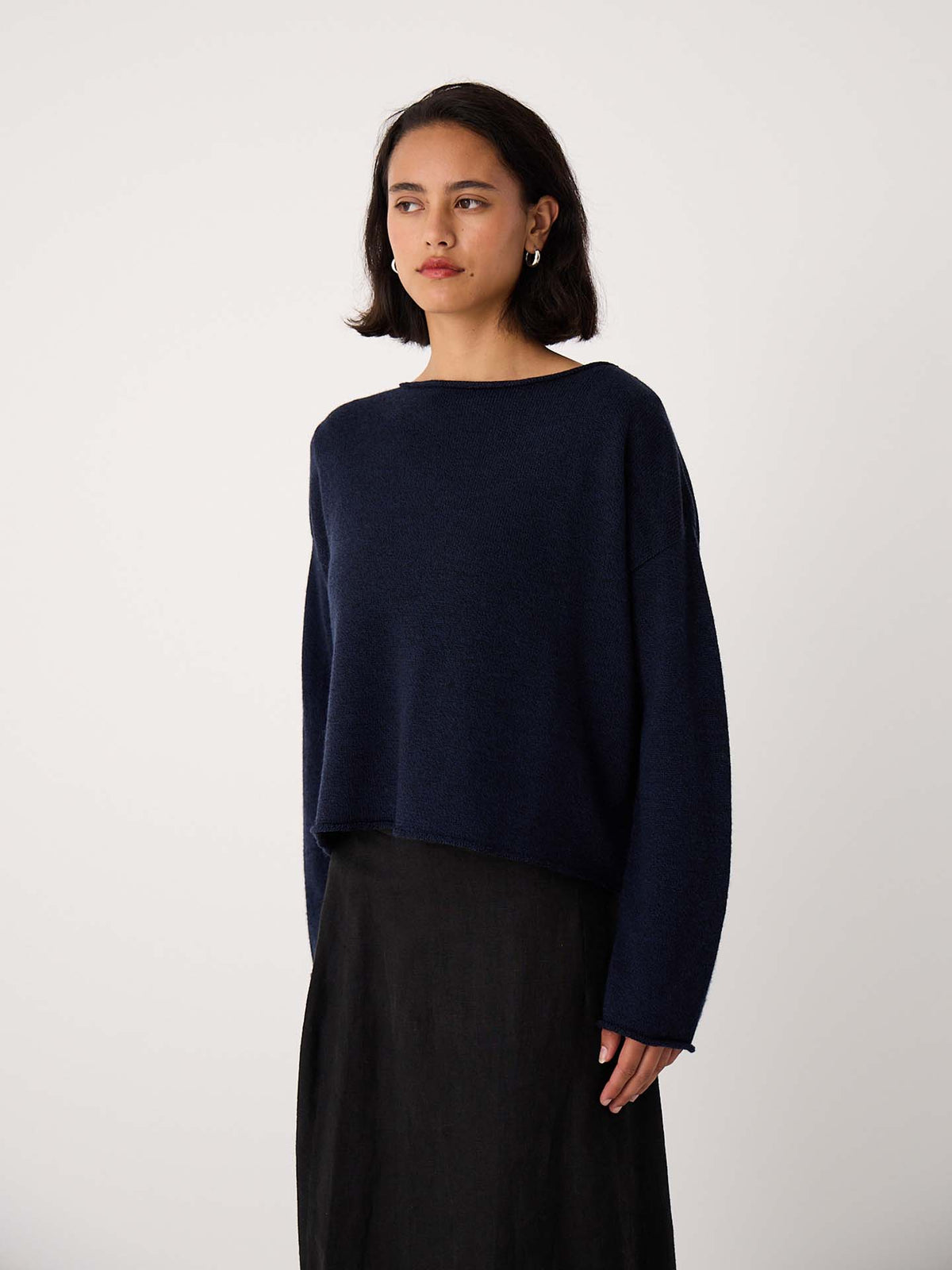 A woman with shoulder-length dark hair is wearing the Doll's Jumper – Ink in a relaxed fit and a black skirt, standing against a plain white background.