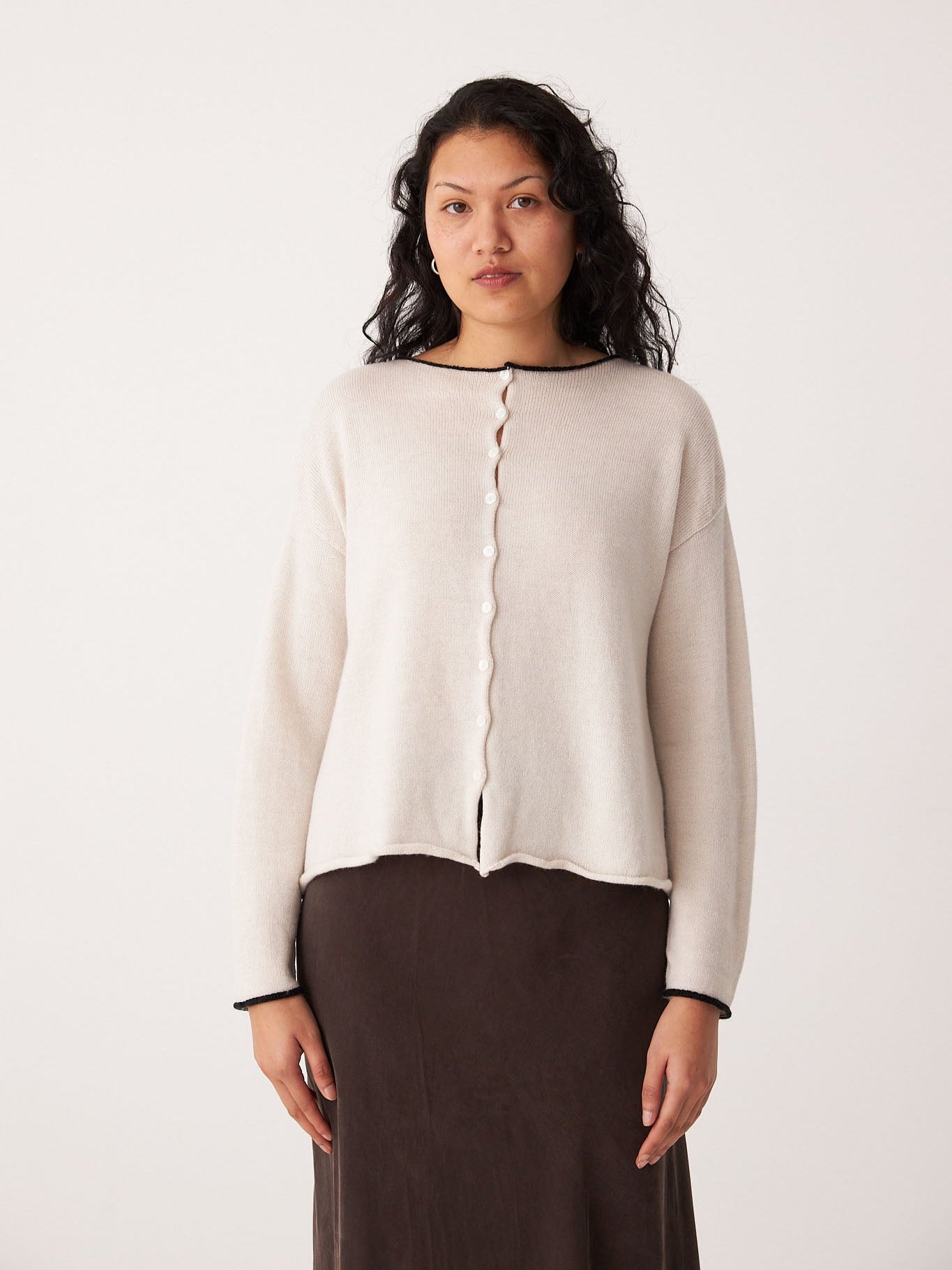 A woman with wavy dark hair models Francie’s Doll's Reversible Cardigan in ivory, paired with a dark brown skirt, cropped style, standing against a plain light background.