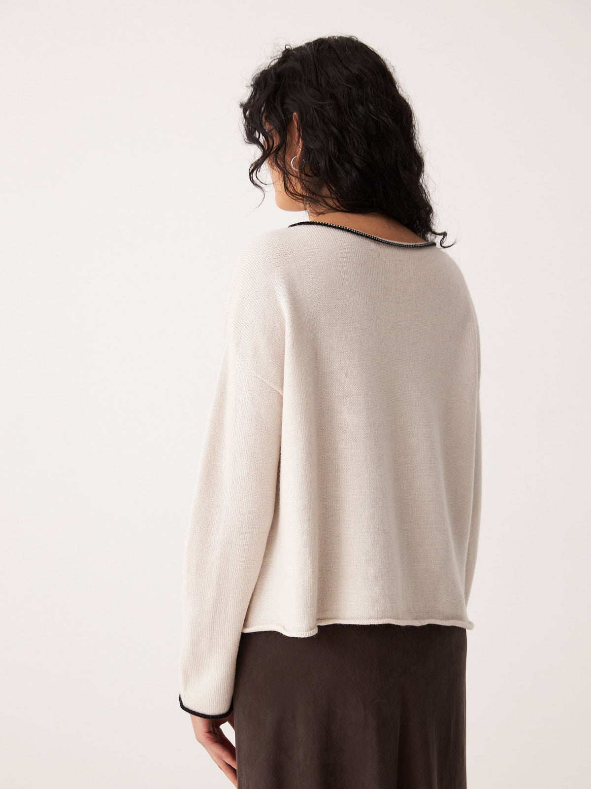 A person with wavy dark hair is shown from the back, wearing Francie’s Doll&#39;s Reversible Cardigan in ivory &amp; black with a dark skirt—a chic look and perfect inspiration for petite fashion.