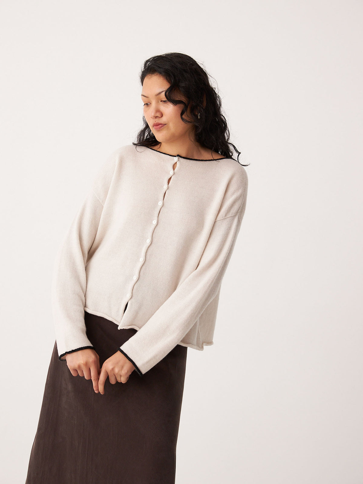 A woman models Francie’s Doll&#39;s Reversible Cardigan in Ivory &amp; Black, a cropped button-up style, paired with a dark skirt against a plain background—an ideal chic choice for petite wardrobes.