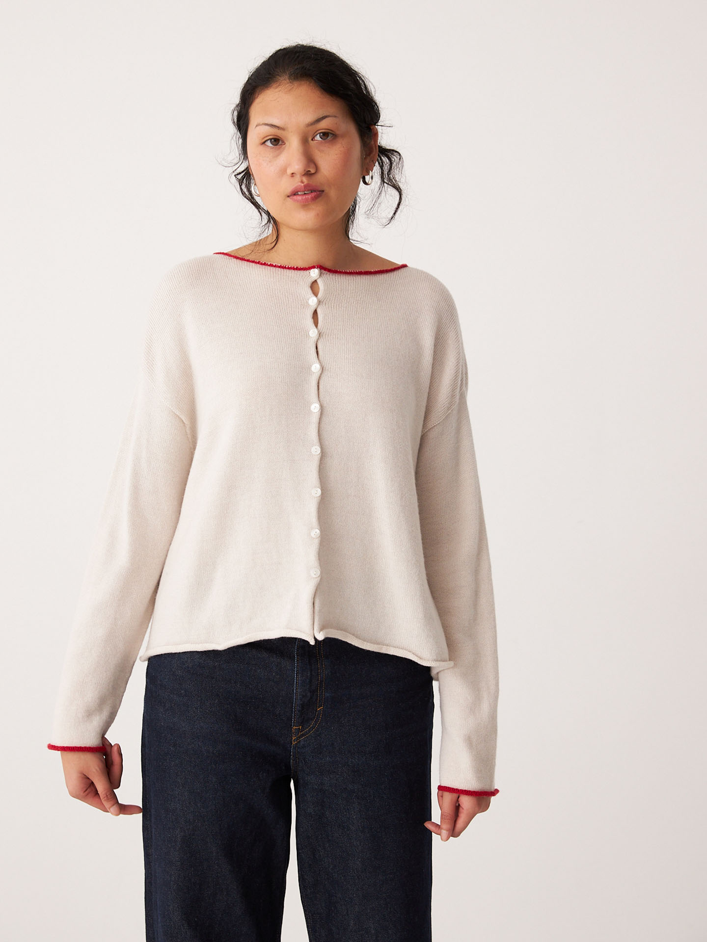 A person models the Francie Doll's Reversible Cardigan in ivory and red with relaxed fit, paired with cropped dark jeans, standing against a plain white background.