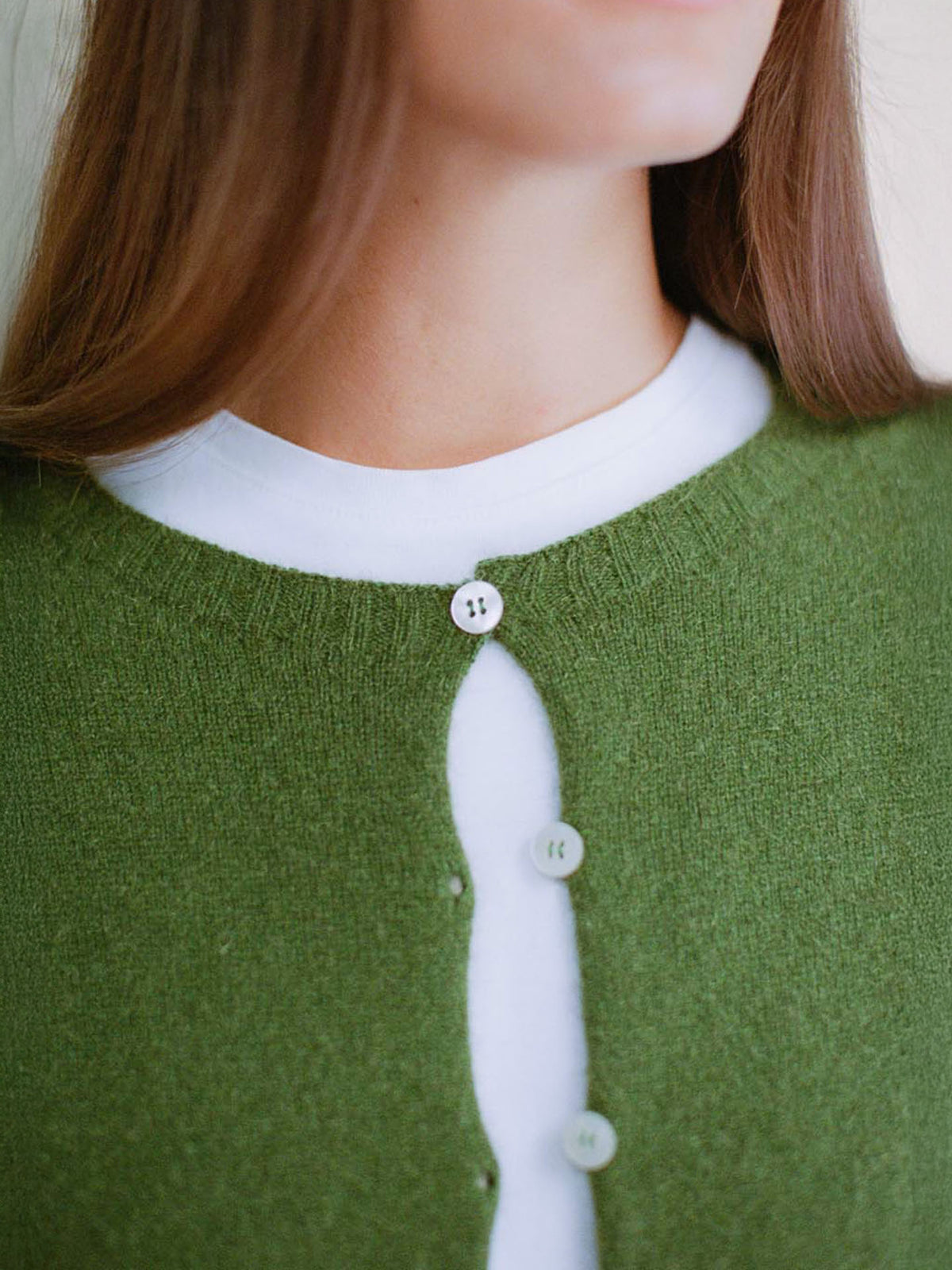 A petite person wears Francie&#39;s Dusk Cardigan in Herb Green—a relaxed-fit, cropped style with just the top button fastened over a white shirt for a cozy look.