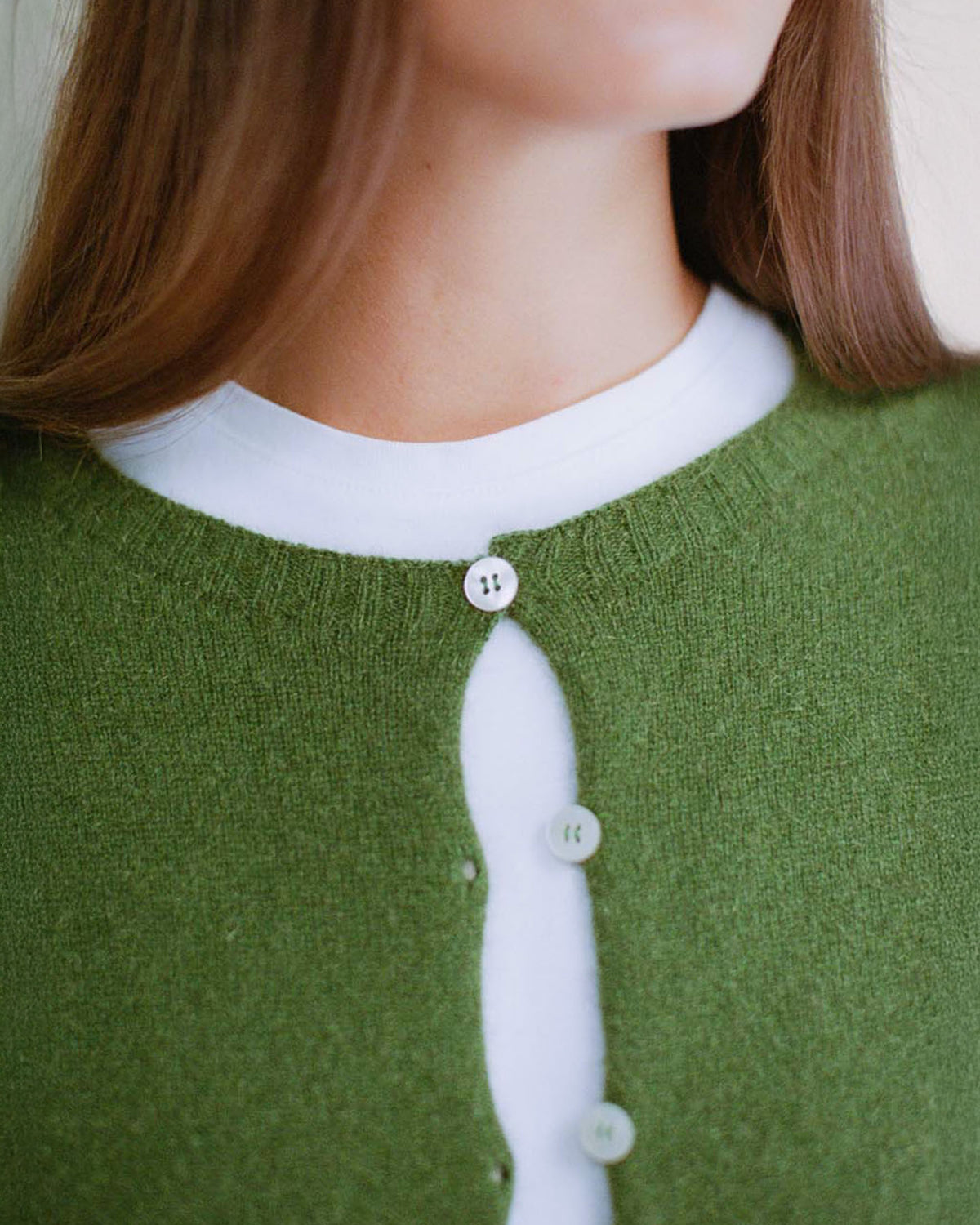 A petite person wears Francie's Dusk Cardigan in Herb Green—a relaxed-fit, cropped style with just the top button fastened over a white shirt for a cozy look.