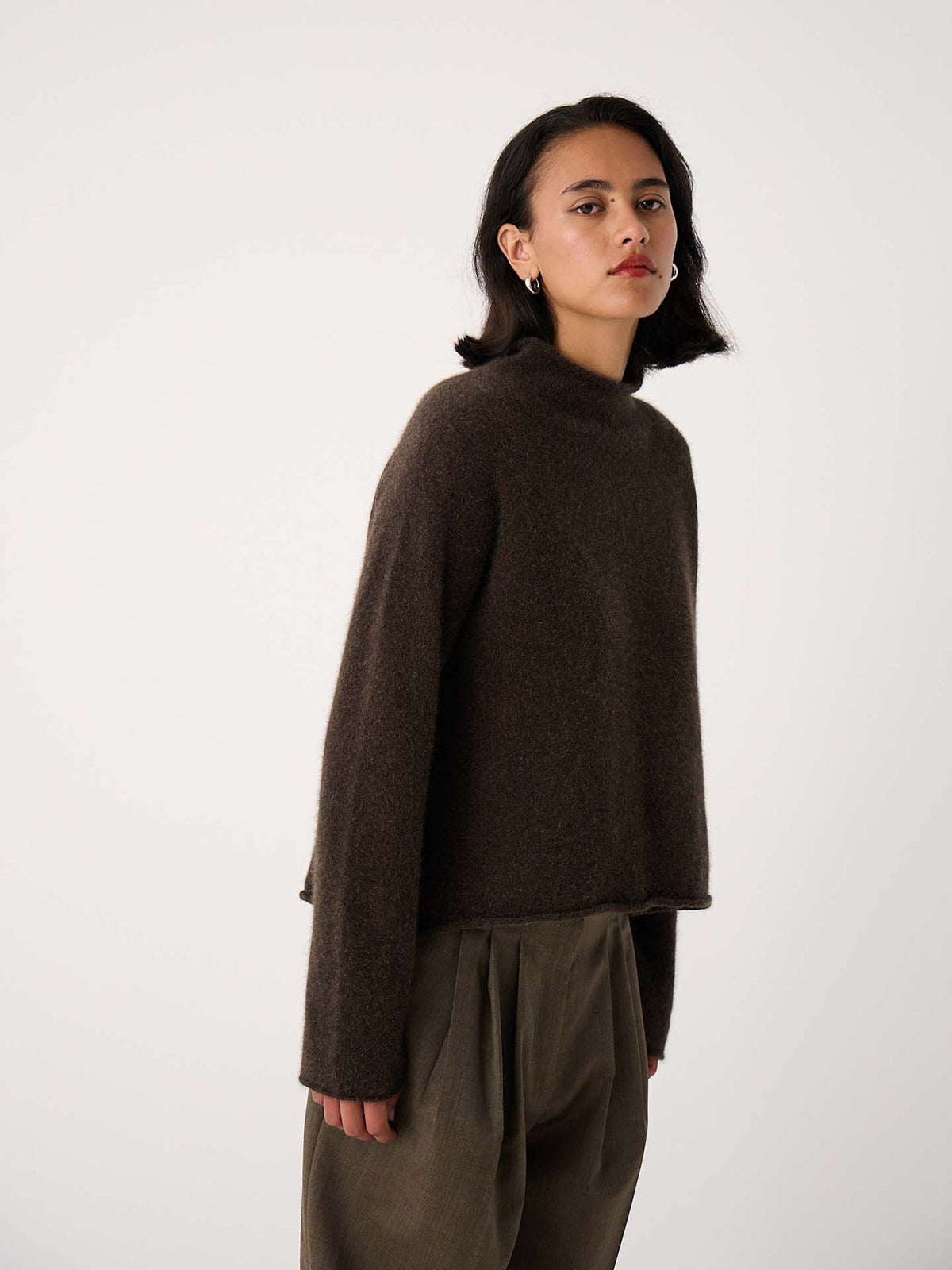 A petite person with short dark hair wears the Eclipse Knit – Truffle, styled in a relaxed, oversized fit against a plain light background.