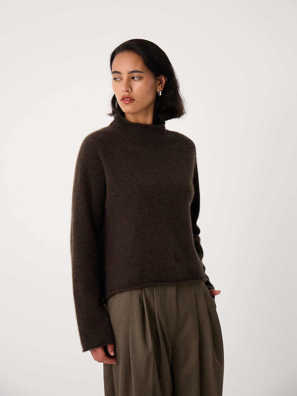 Petite woman wearing the Eclipse Knit – Truffle, a dark brown, relaxed-fit long-sleeve sweater, paired with wide-leg khaki pants, standing against a plain white background.