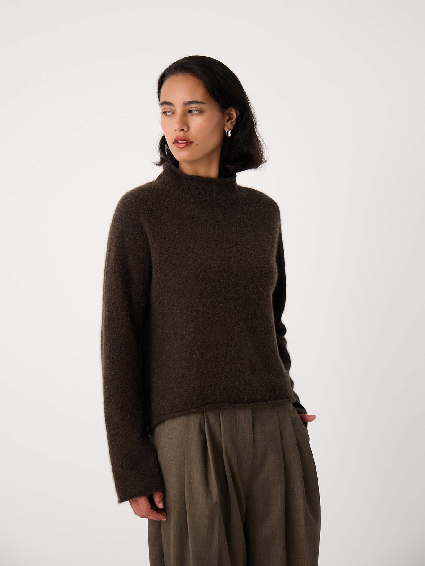 Petite woman wearing the Eclipse Knit – Truffle, a dark brown, relaxed-fit long-sleeve sweater, paired with wide-leg khaki pants, standing against a plain white background.