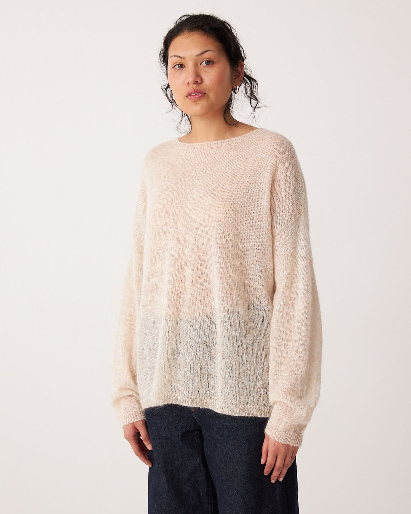 A person stands facing forward, wearing the Feather Knit – Creme oversized sweater with a relaxed fit and dark pants, against a plain white background.