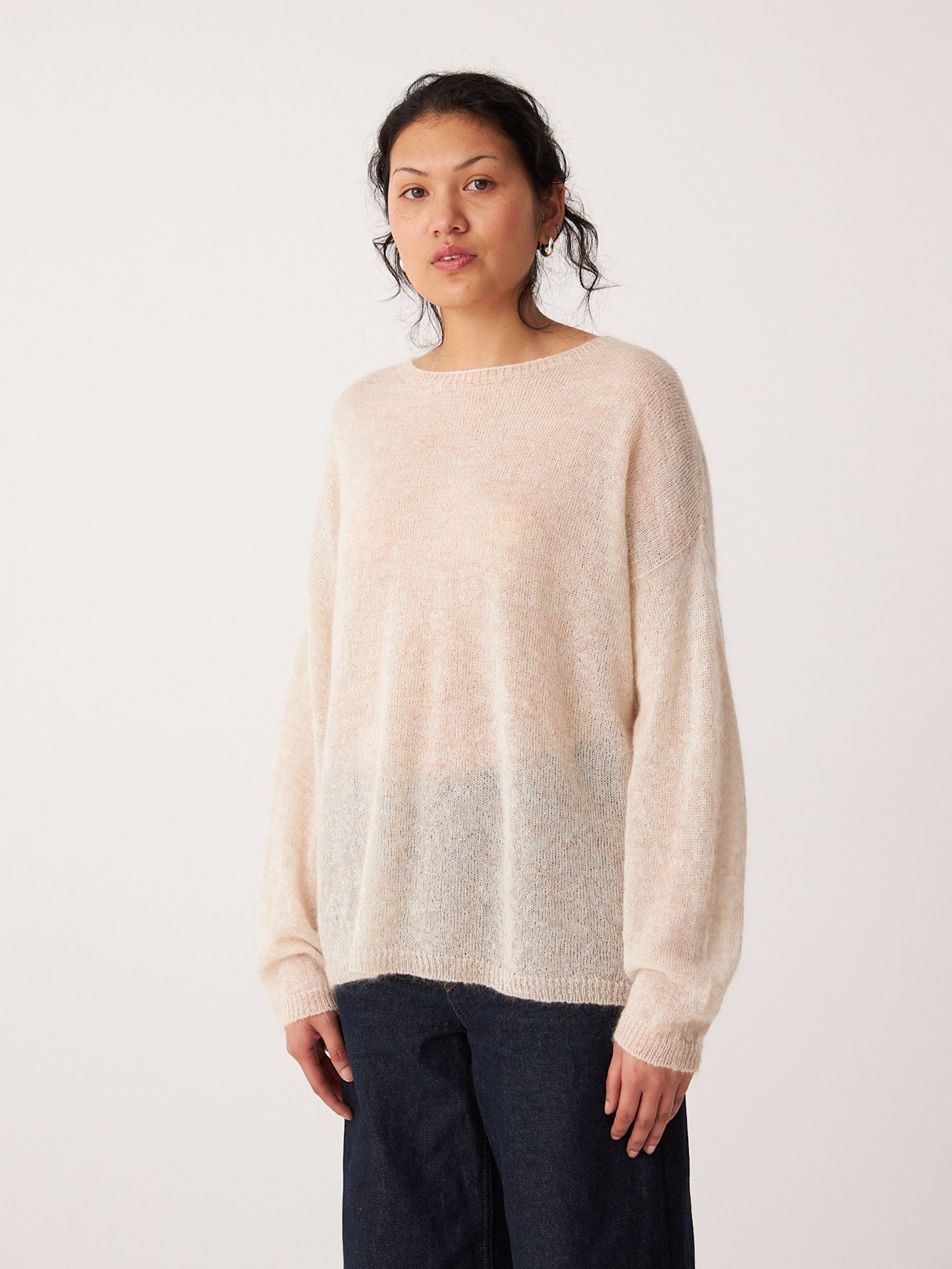 A person stands facing forward, wearing the Feather Knit – Creme oversized sweater with a relaxed fit and dark pants, against a plain white background.