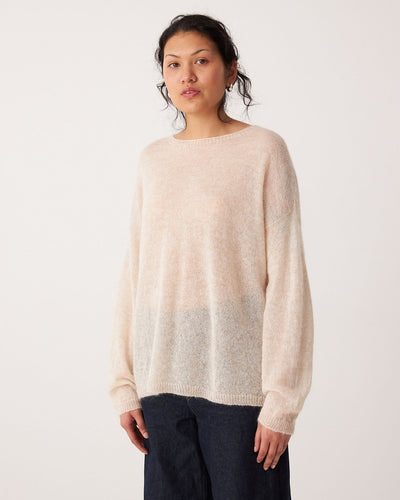 A person stands facing forward, wearing the Feather Knit – Creme oversized sweater with a relaxed fit and dark pants, against a plain white background.
