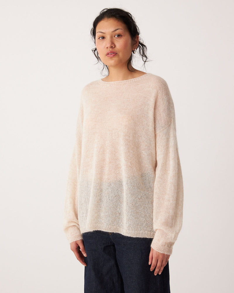 A person stands facing forward, wearing the Feather Knit – Creme oversized sweater with a relaxed fit and dark pants, against a plain white background.
