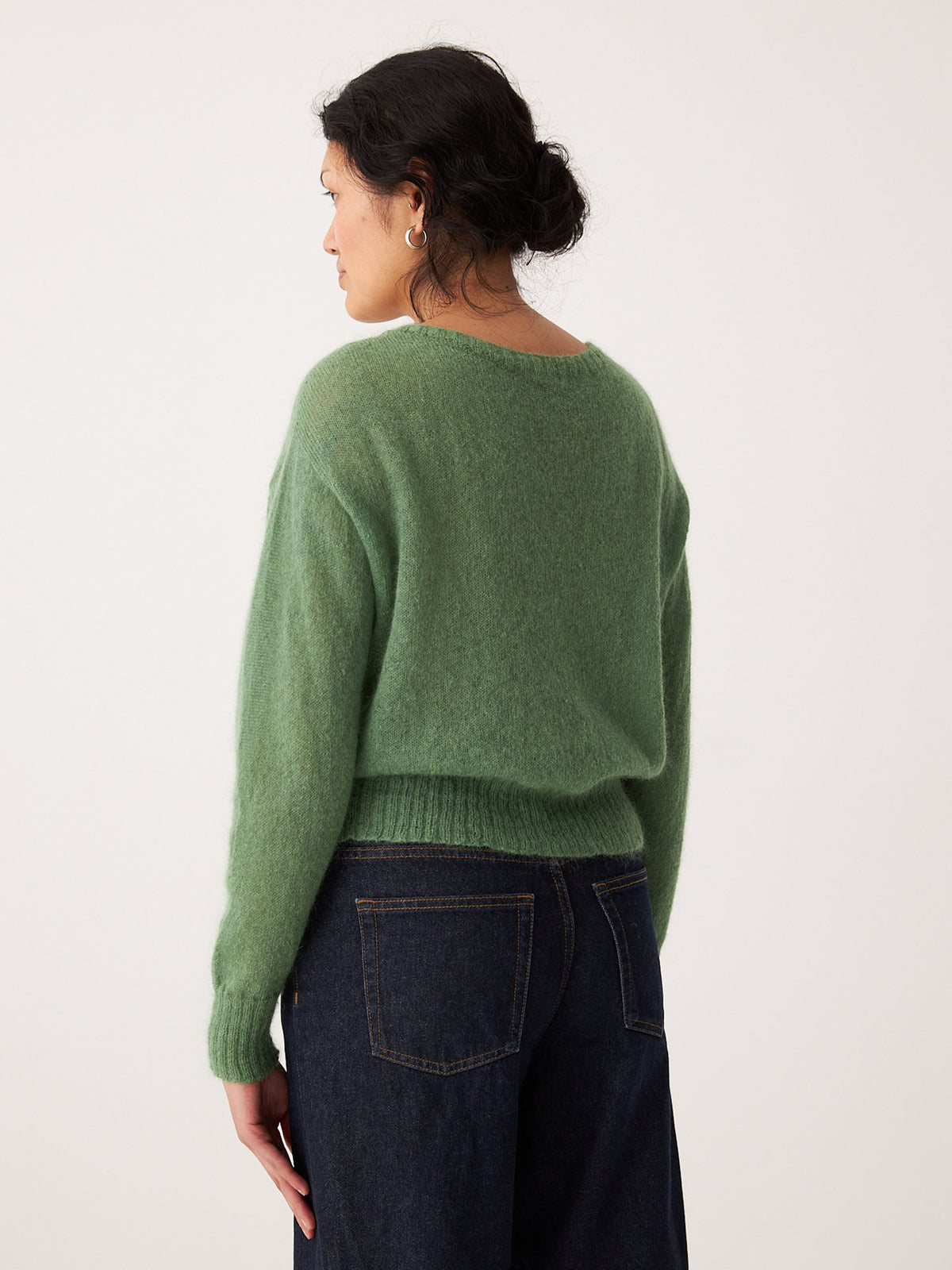 A woman wears the Fleur Cardigan in Clover, a green sweater with a relaxed fit.