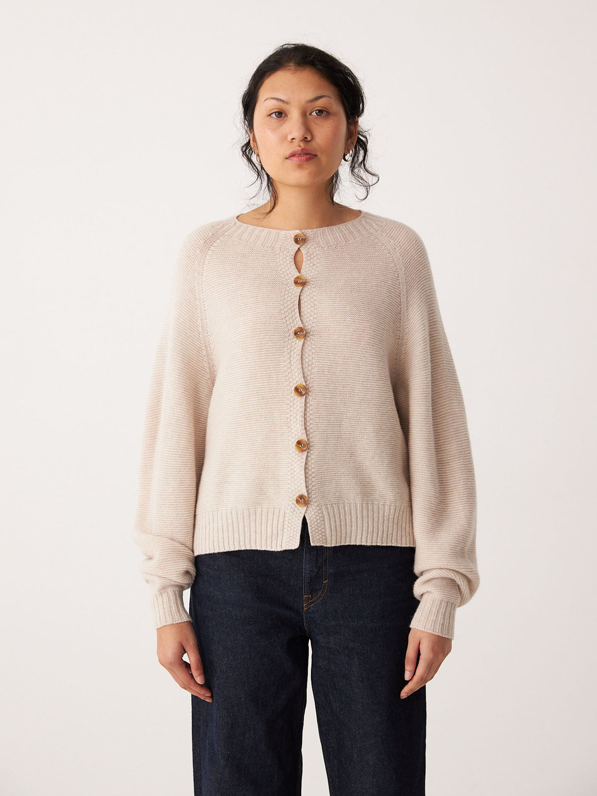 A person stands facing forward, wearing the Francie Garter Loft Cardigan in Creme and dark jeans against a plain white background.