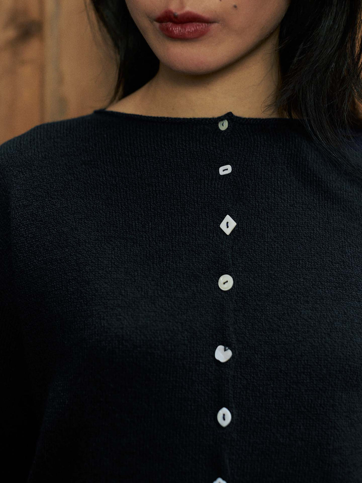 Close-up of a person wearing the Heirloom Doll's Cardigan – Black, a relaxed-fit textured shirt accented with uniquely shaped white buttons vertically down the front.