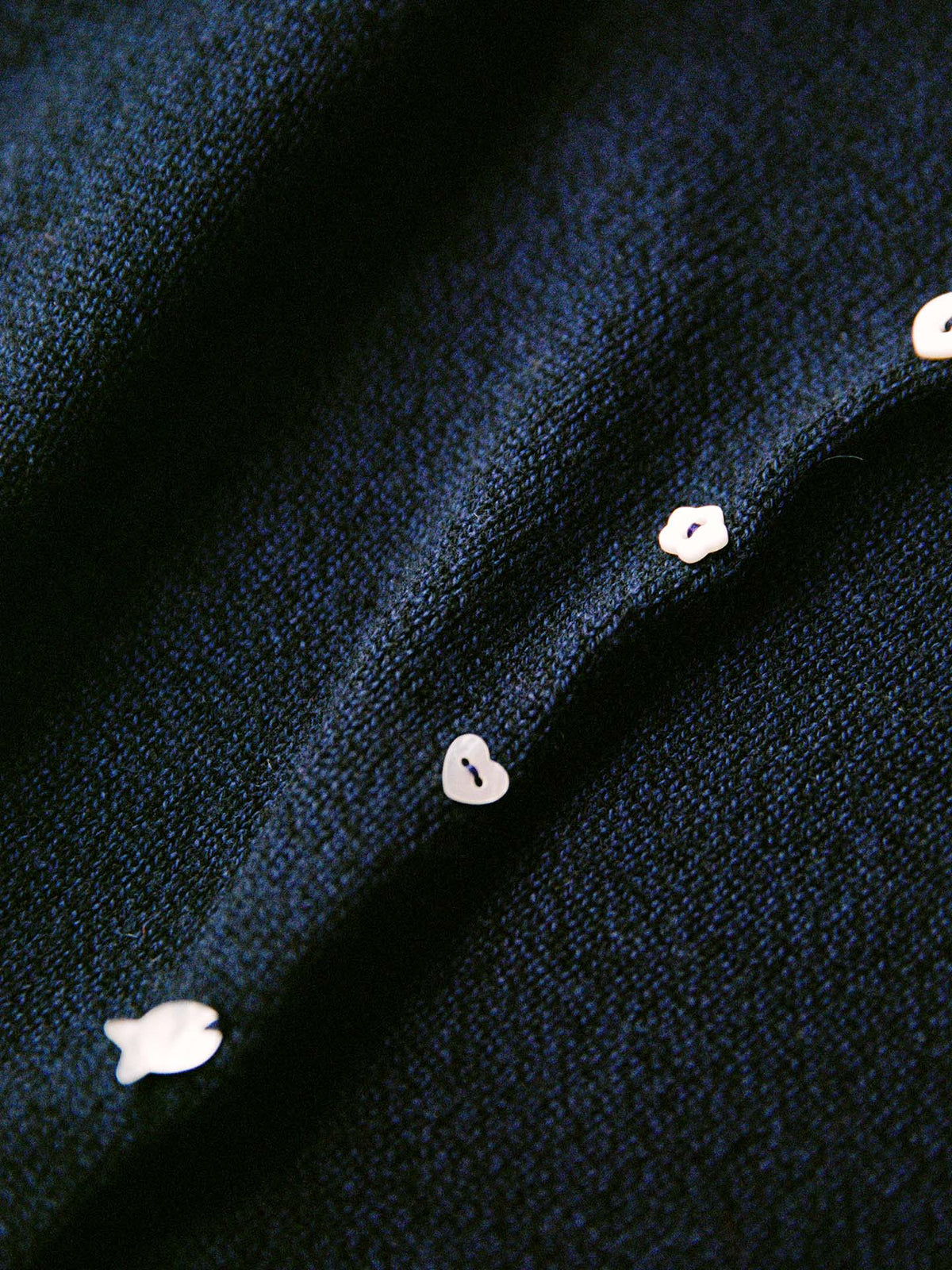 Close-up of the Heirloom Doll's Cardigan – Ink featuring dark textured fabric and small white buttons along the seam, ideal for a relaxed or petite cropped fit—see size guide for more details.