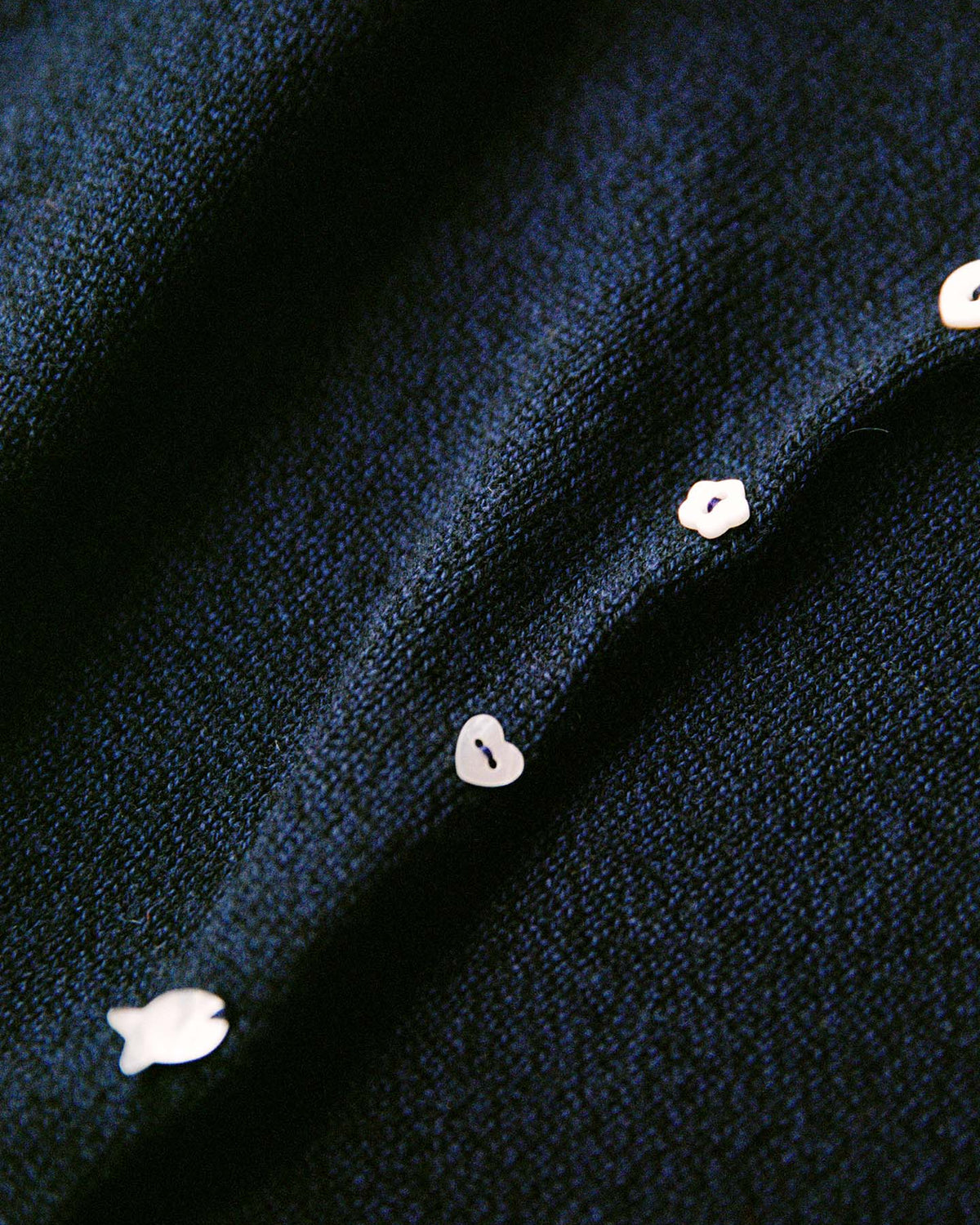 Close-up of the Heirloom Doll's Cardigan – Ink featuring dark textured fabric and small white buttons along the seam, ideal for a relaxed or petite cropped fit—see size guide for more details.