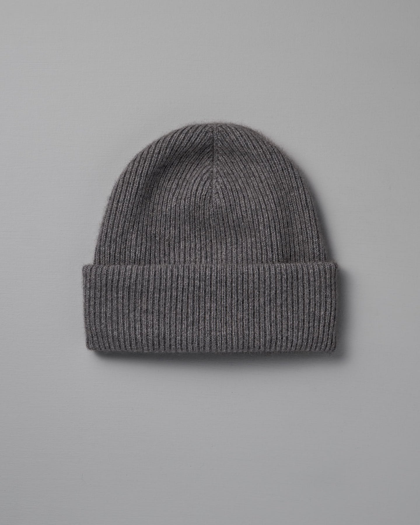 The Hinoki Beanie – Granite, a gray ribbed knit beanie with a folded brim, is laid flat on a light gray background.