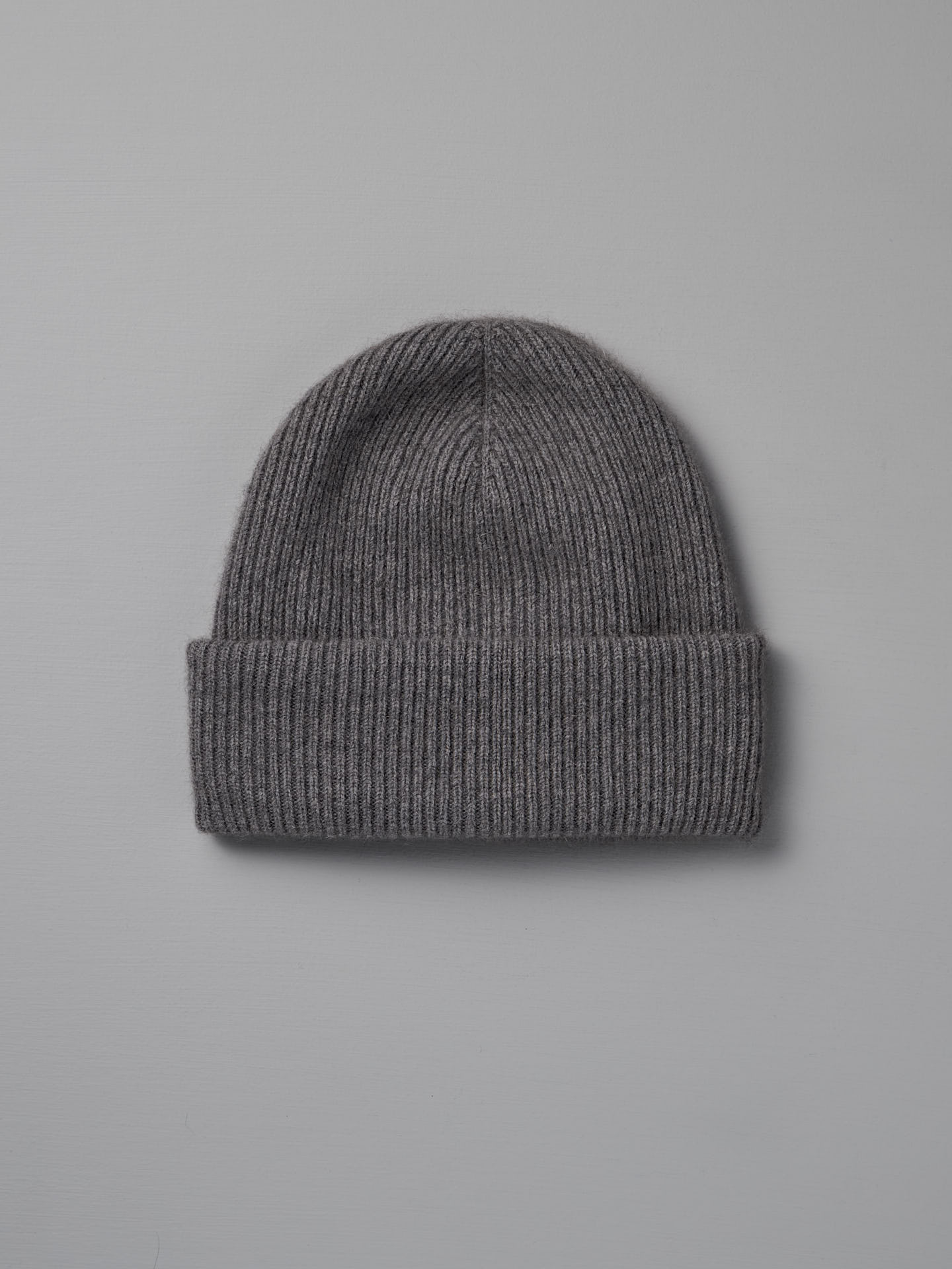 The Hinoki Beanie – Granite, a gray ribbed knit beanie with a folded brim, is laid flat on a light gray background.